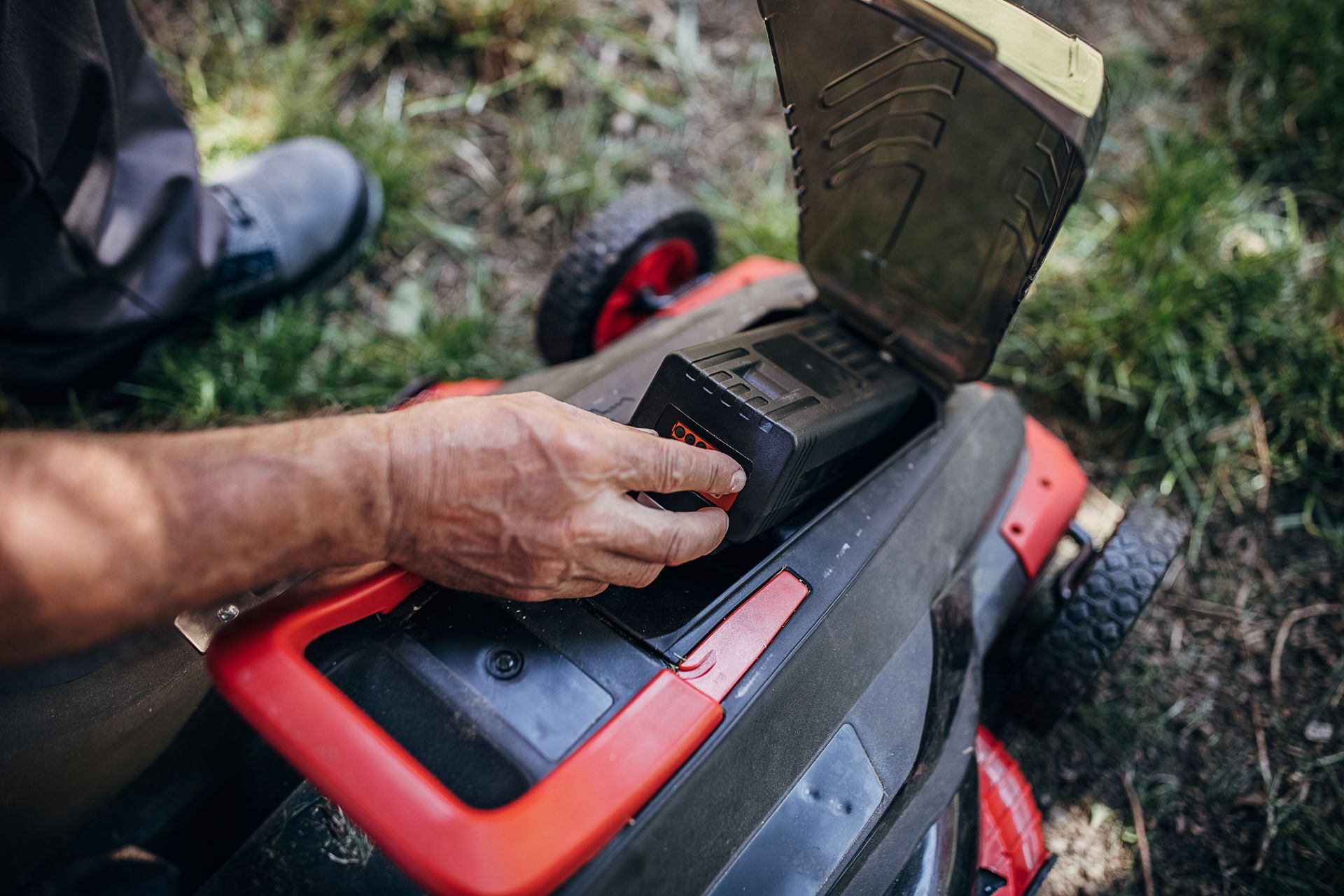 A man is putting a battery into a lawn mower.
