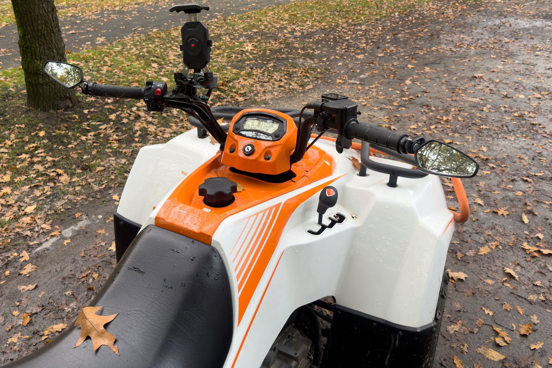 A white and orange atv is parked on a wet road. A white and orange atv is parked on a wet road.