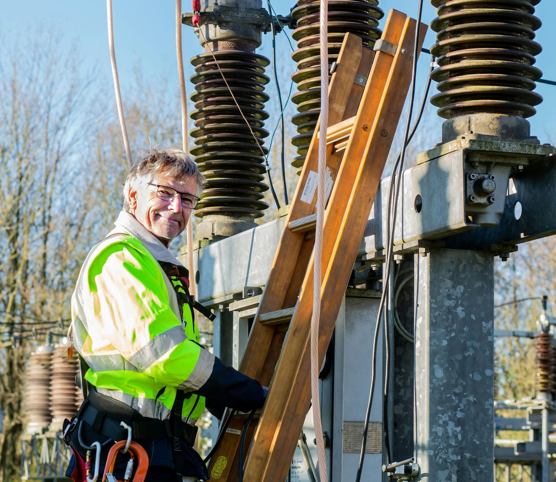 Worker in a neon safety jacket climbing a ladder on outdoor electrical equipment.