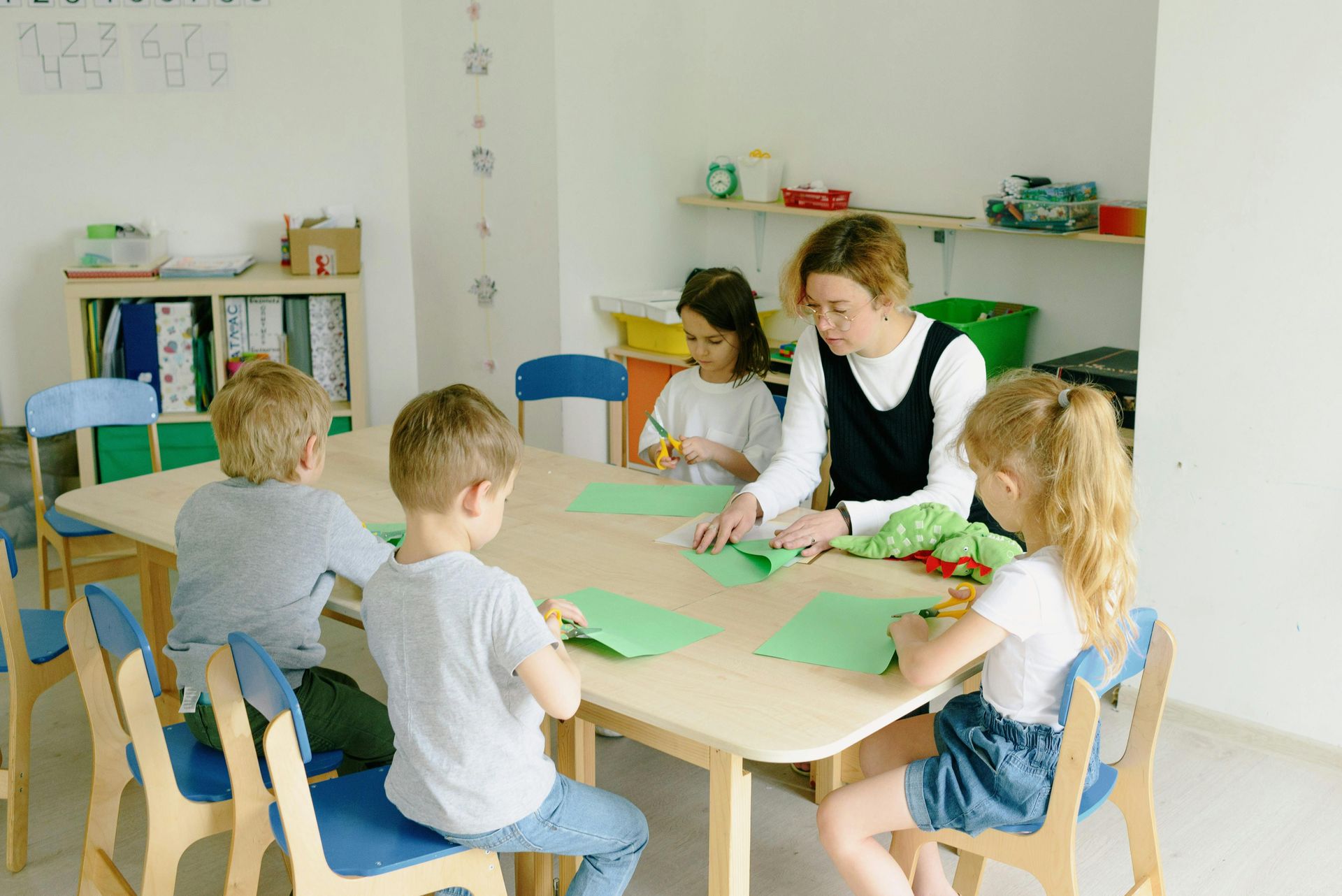 Teacher helping children with crafts at a table in a bright classroom