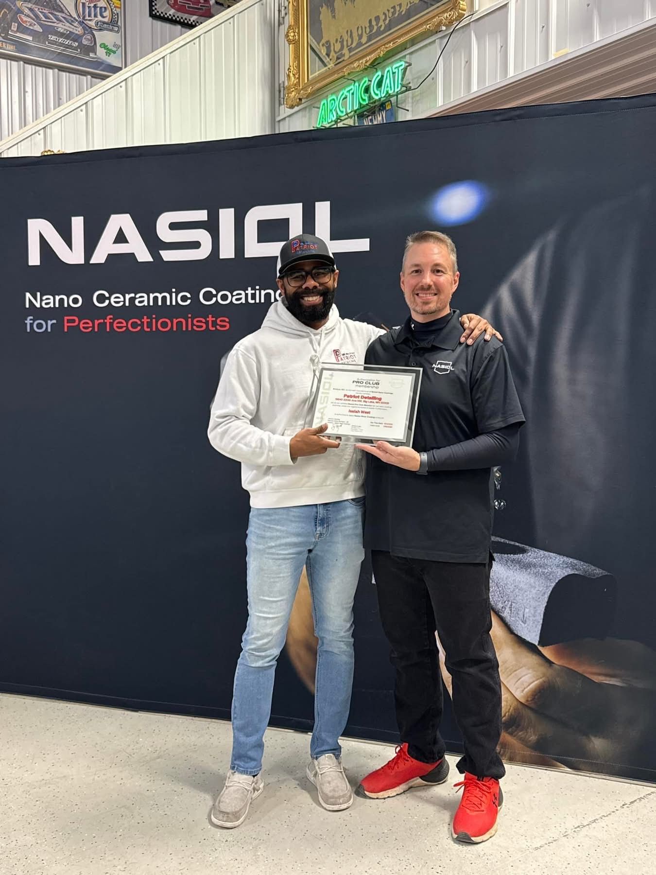 Two men are standing next to each other in front of a wall holding a certificate.