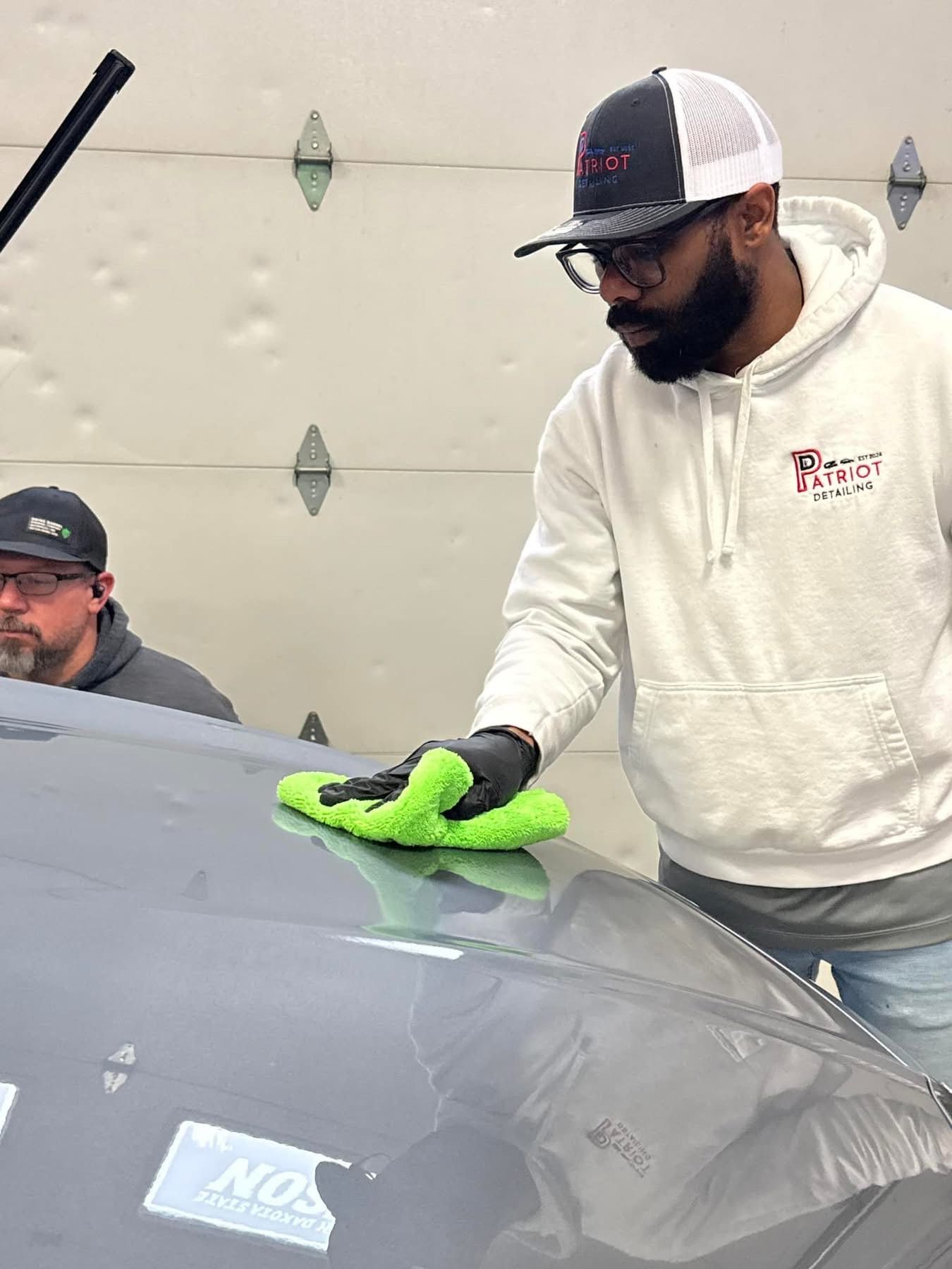A man is cleaning the windshield of a car with a green cloth.