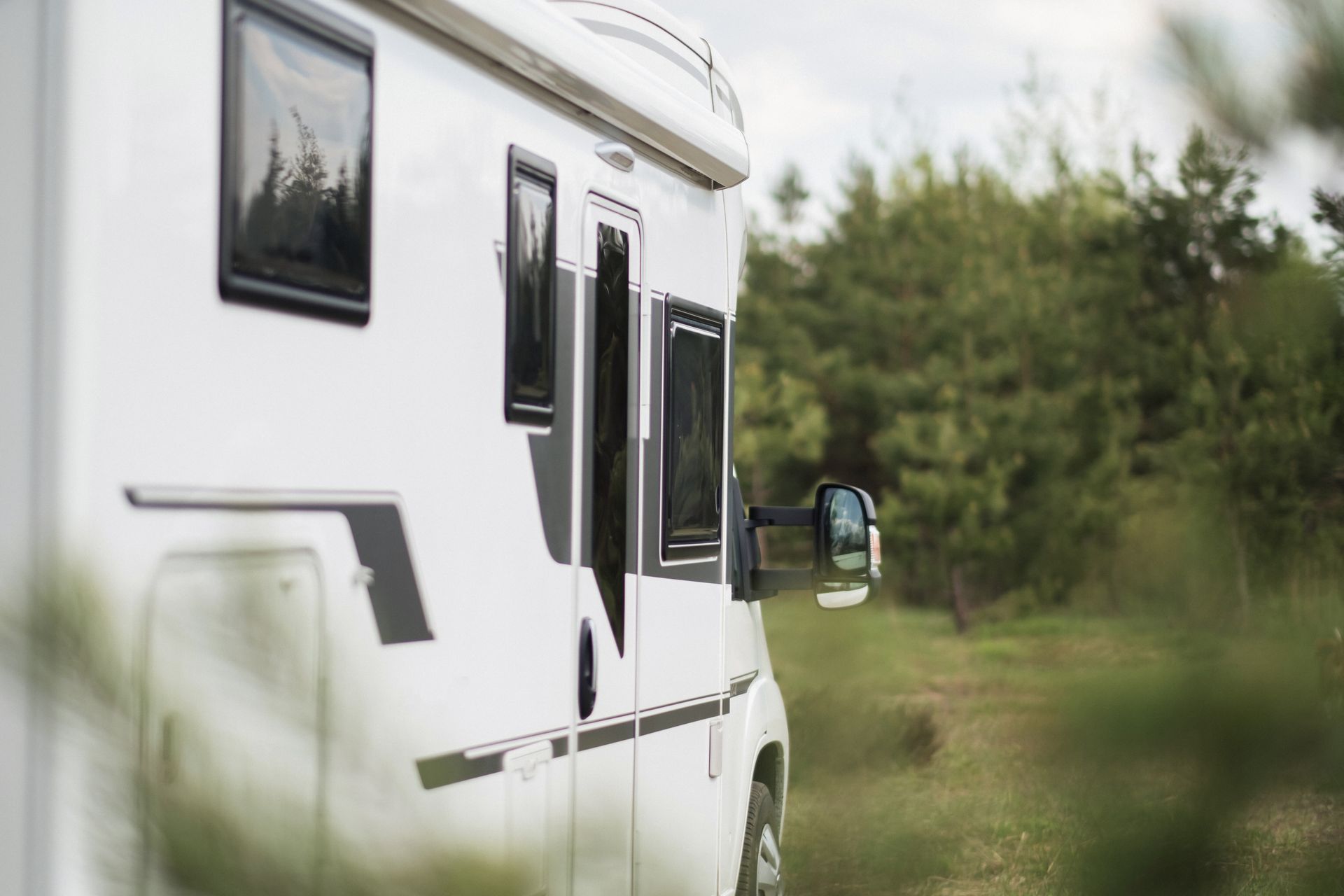 White RV parked in a natural setting, windows open, surrounded by trees.
