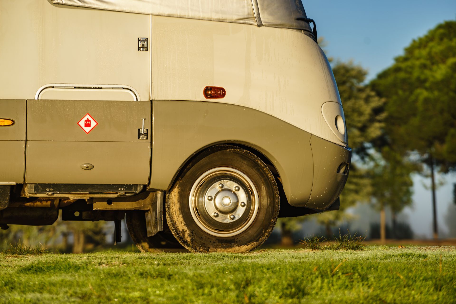 Side view of a light gray RV parked on a grassy field; front tire is visible.