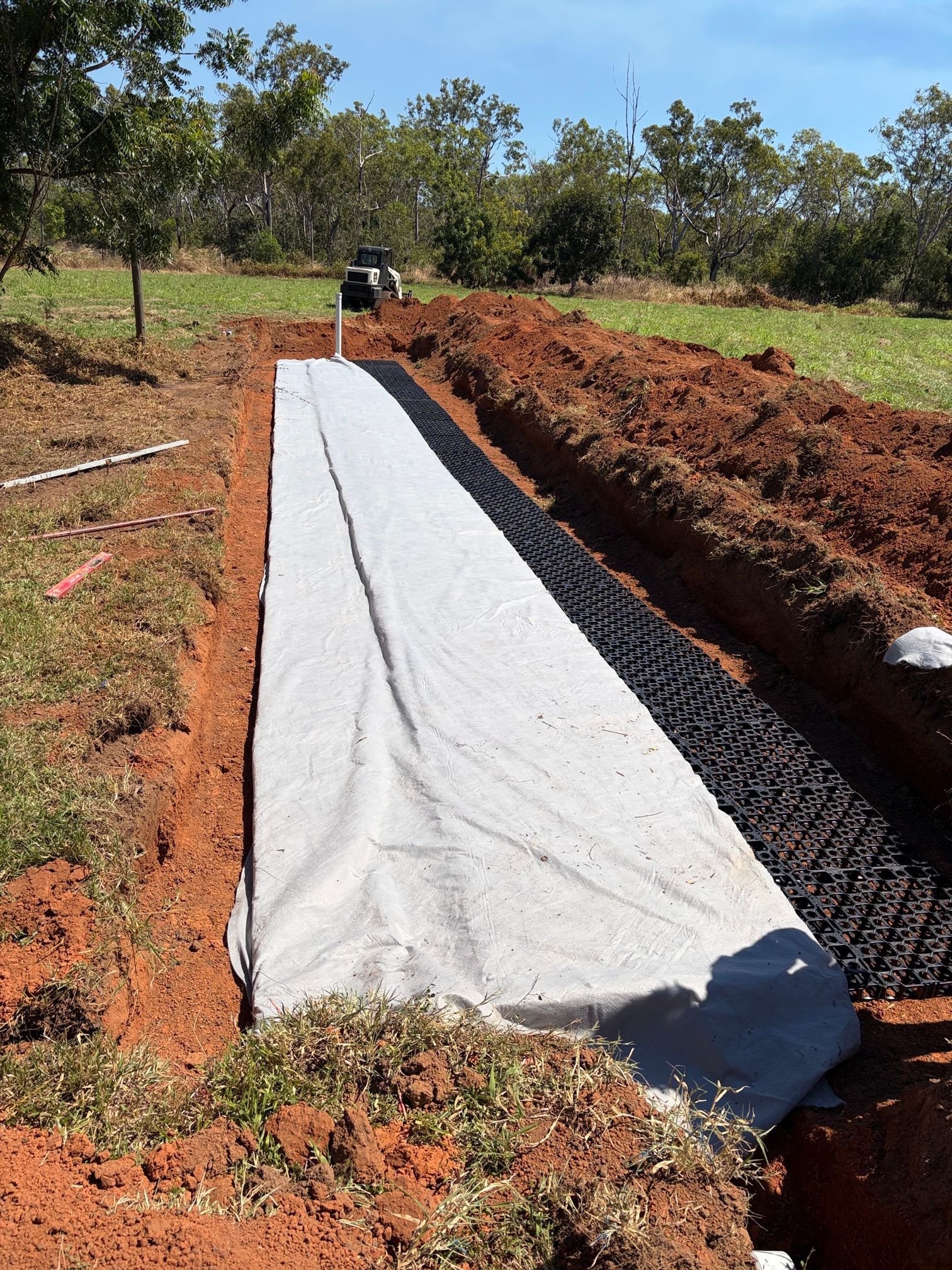 Long white geotextile liner laid in a narrow trench on a dirt construction site outdoors — Tap & Drain Doctor NT in Winnellie, NT