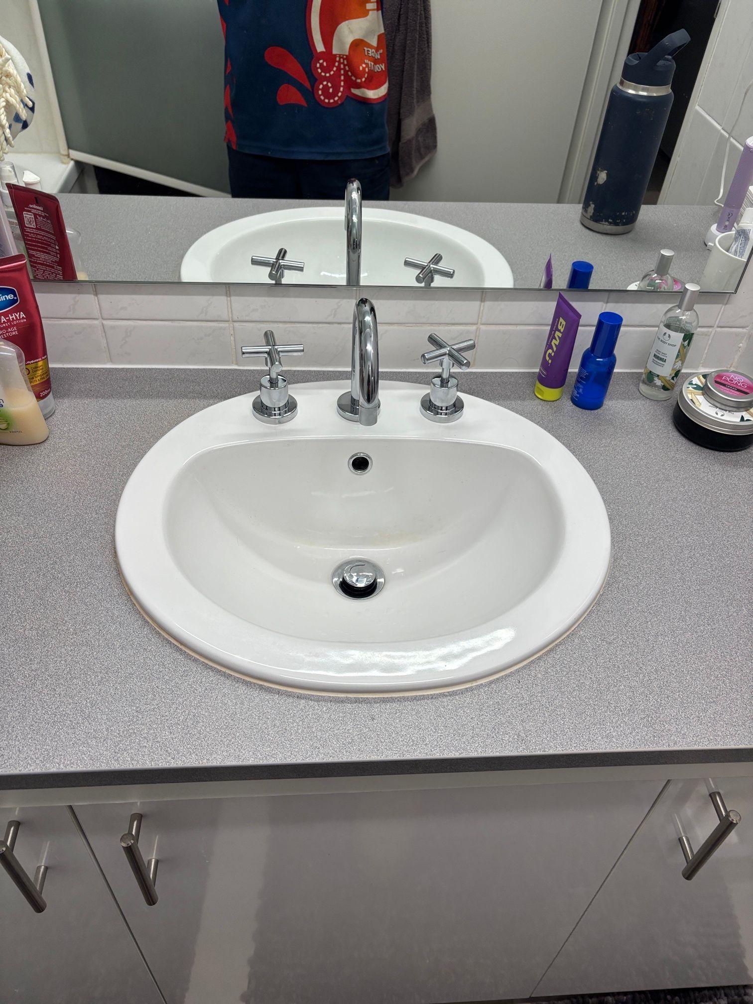 Bathroom sink with mirror, gray countertop, and assorted toiletries on the vanity sides — Tap & Drain Doctor NT in Winnellie, NT