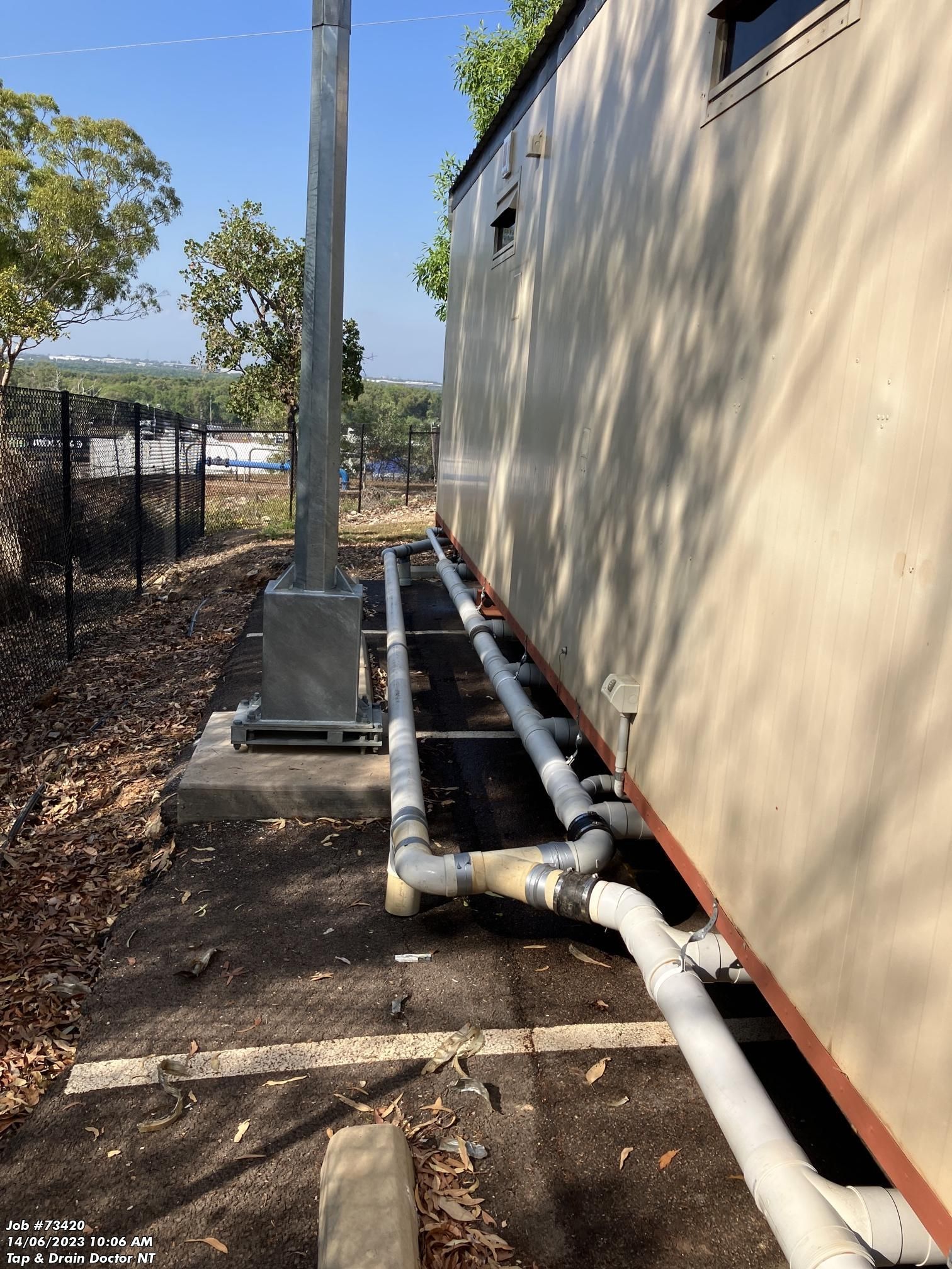 Outdoor utility pipes running alongside a beige building on a sunny path near a fence — Tap & Drain Doctor NT in Winnellie, NT