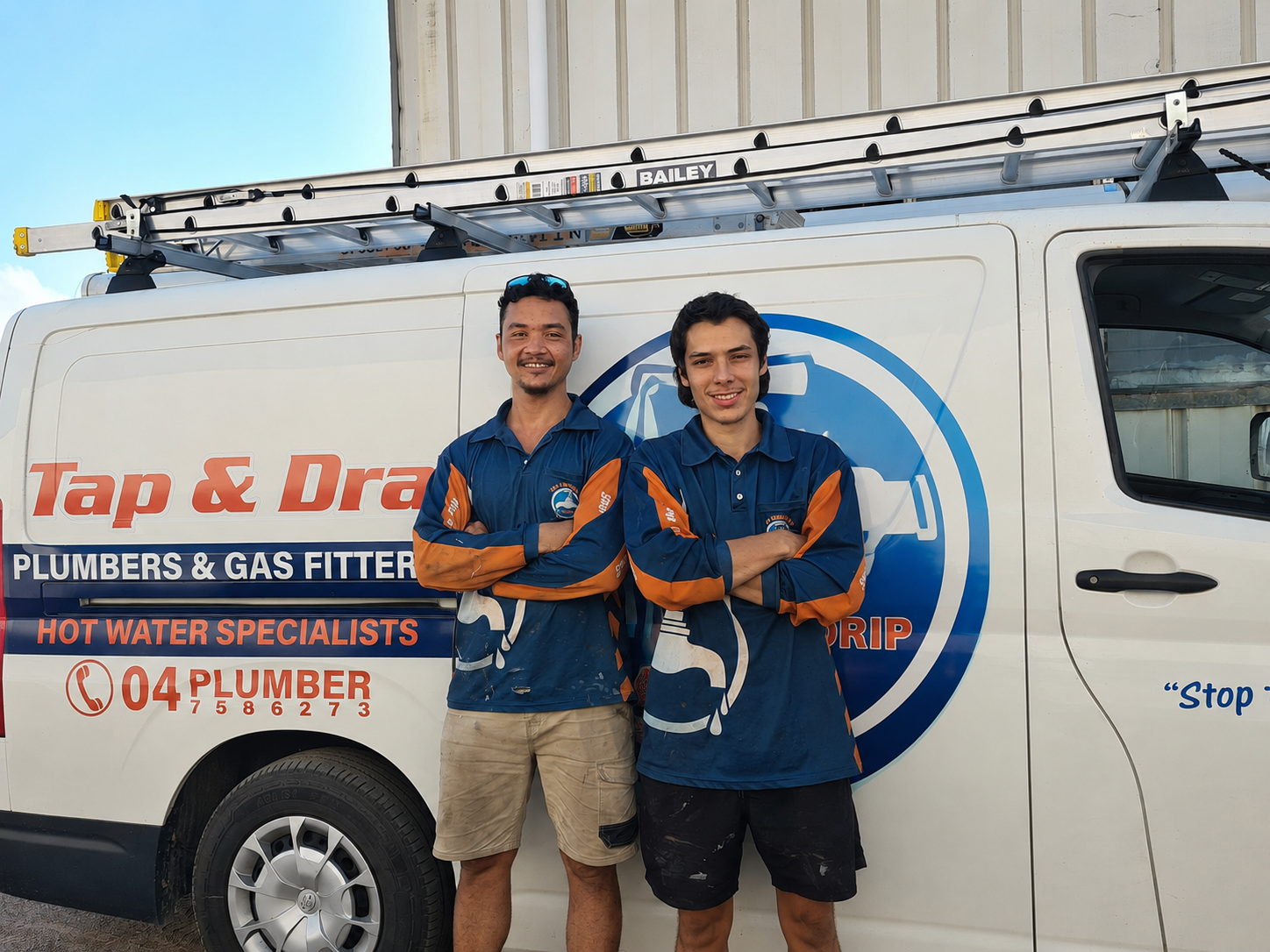 Two smiling workers in blue uniforms standing beside a Tap & Drain plumbing service van — Tap & Drain Doctor NT in Winnellie, NT