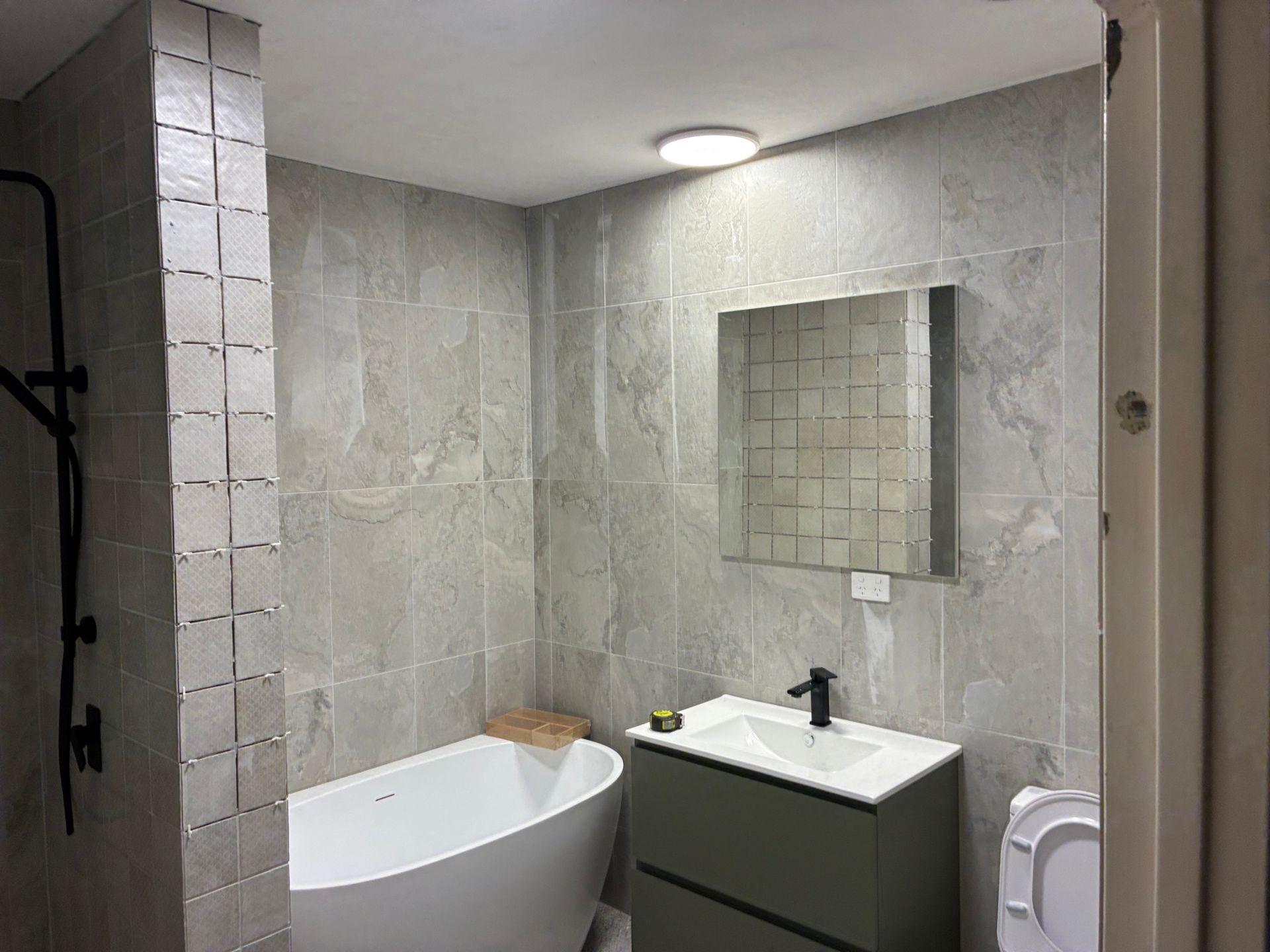 Modern bathroom with tiled walls, oval tub, sink vanity, mirror, and toilet paper holder — Tap & Drain Doctor NT in Winnellie, NT