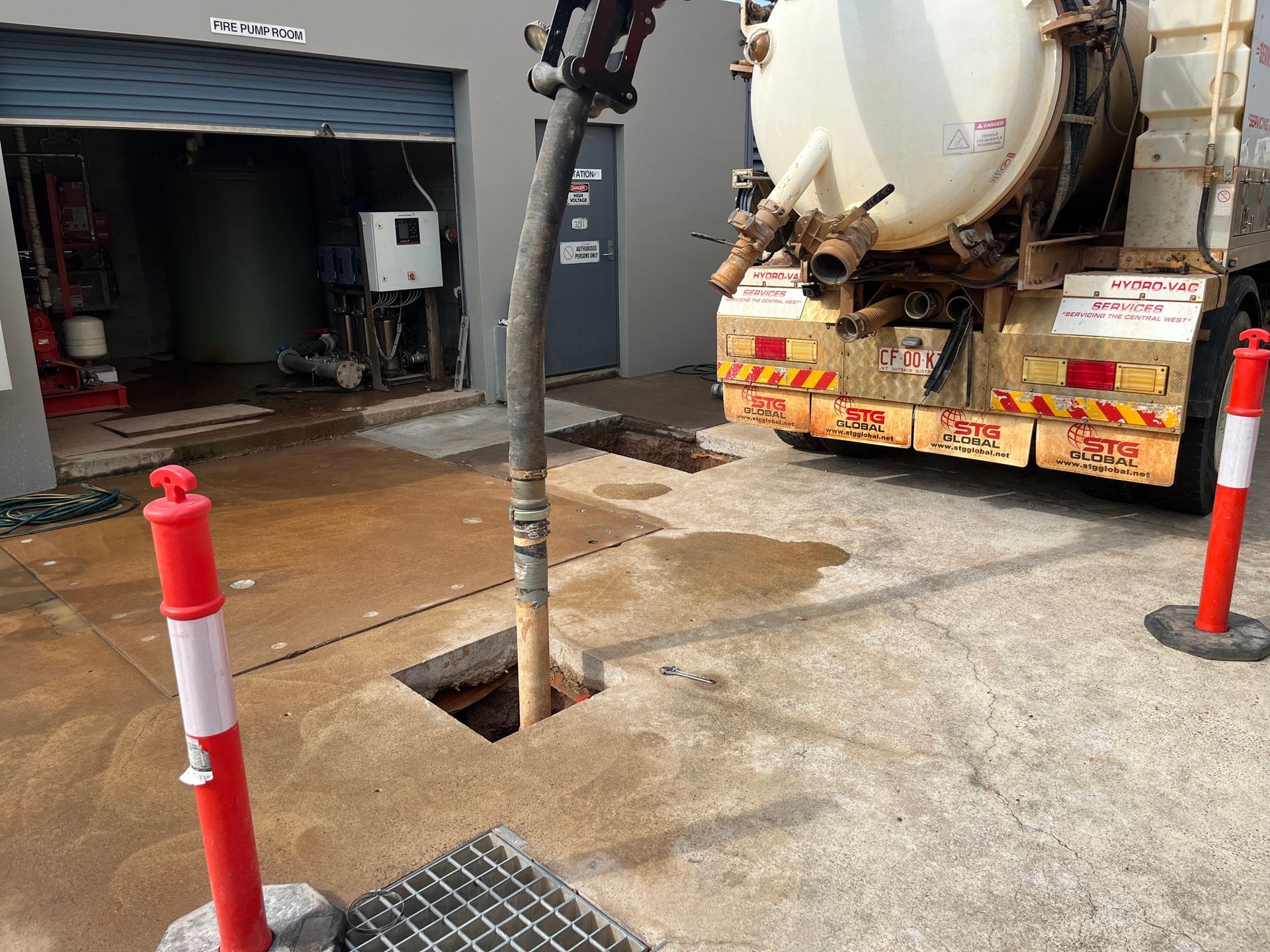 Concrete yard with open utility hatch, truck, and tanker parked beside an industrial building — Tap & Drain Doctor NT in Winnellie, NT