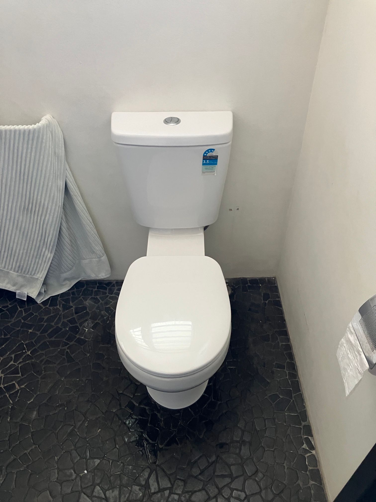 Small white toilet in a narrow bathroom with black floor tile and white walls — Tap & Drain Doctor NT in Winnellie, NT