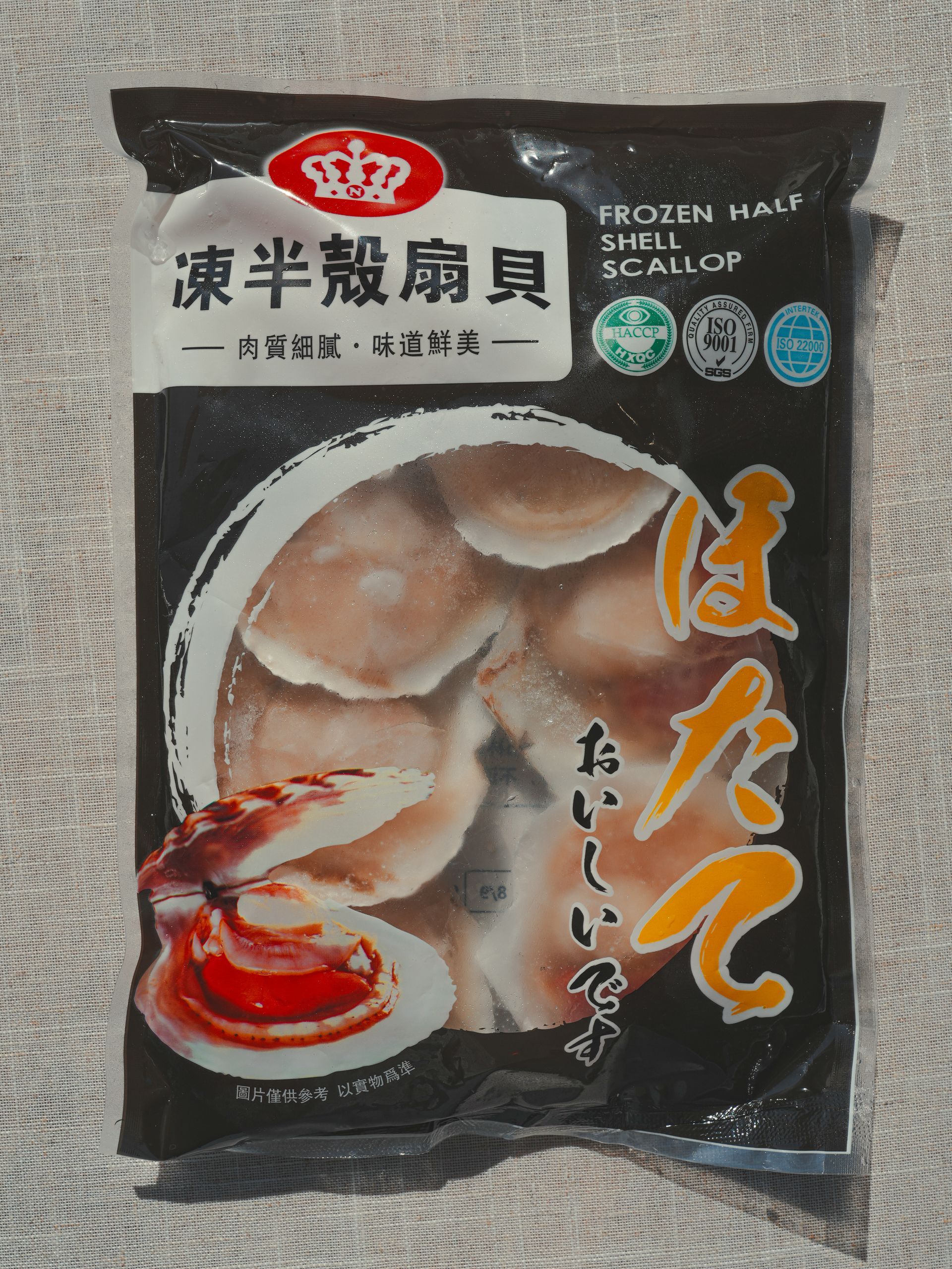 扇貝盛於黑色盤子上，配上番茄和檸檬。木桌，棕櫚葉。