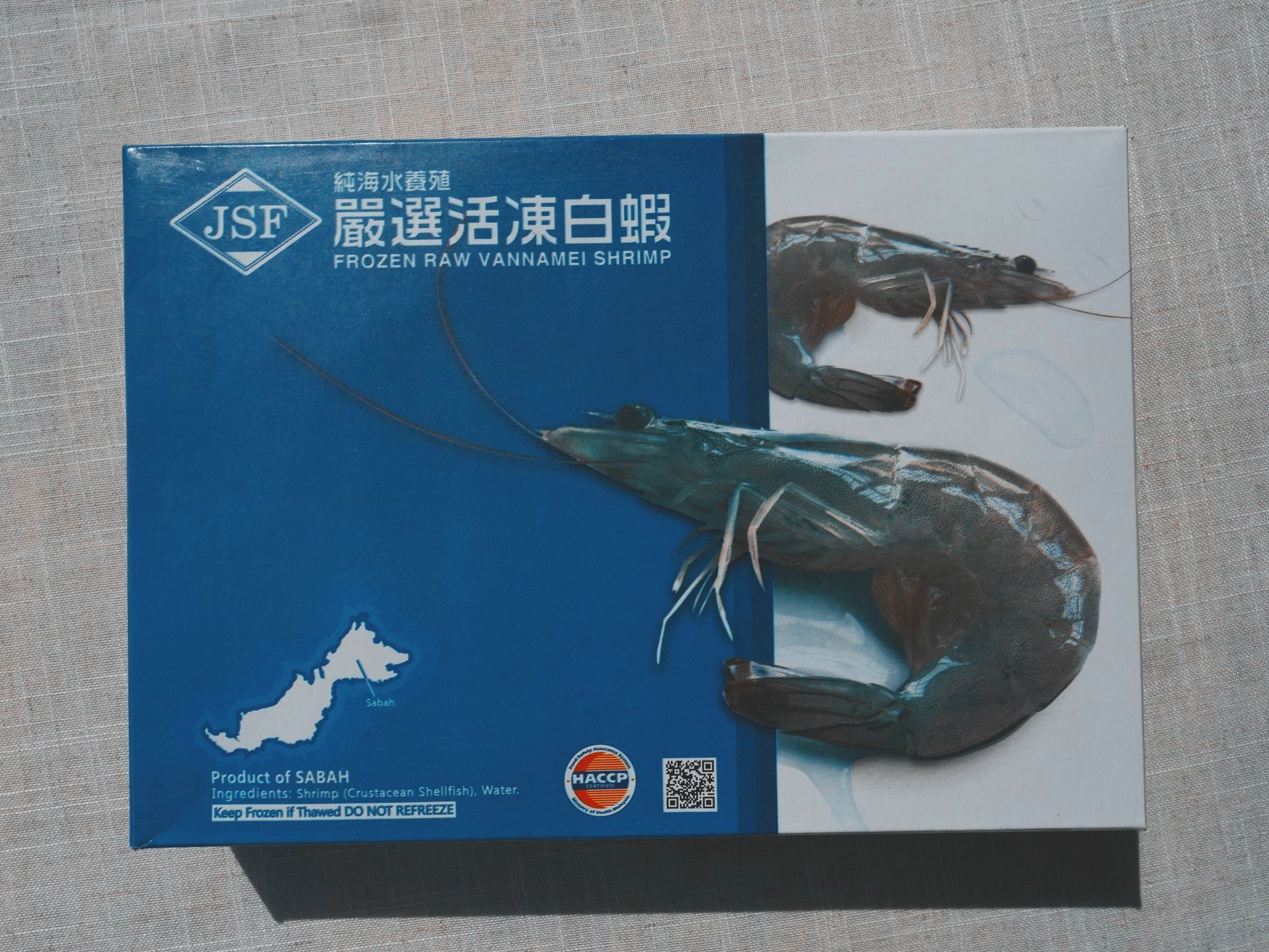 一盒冷凍蝦，盒蓋是藍白的。盒子裡裝著很多熟蝦。