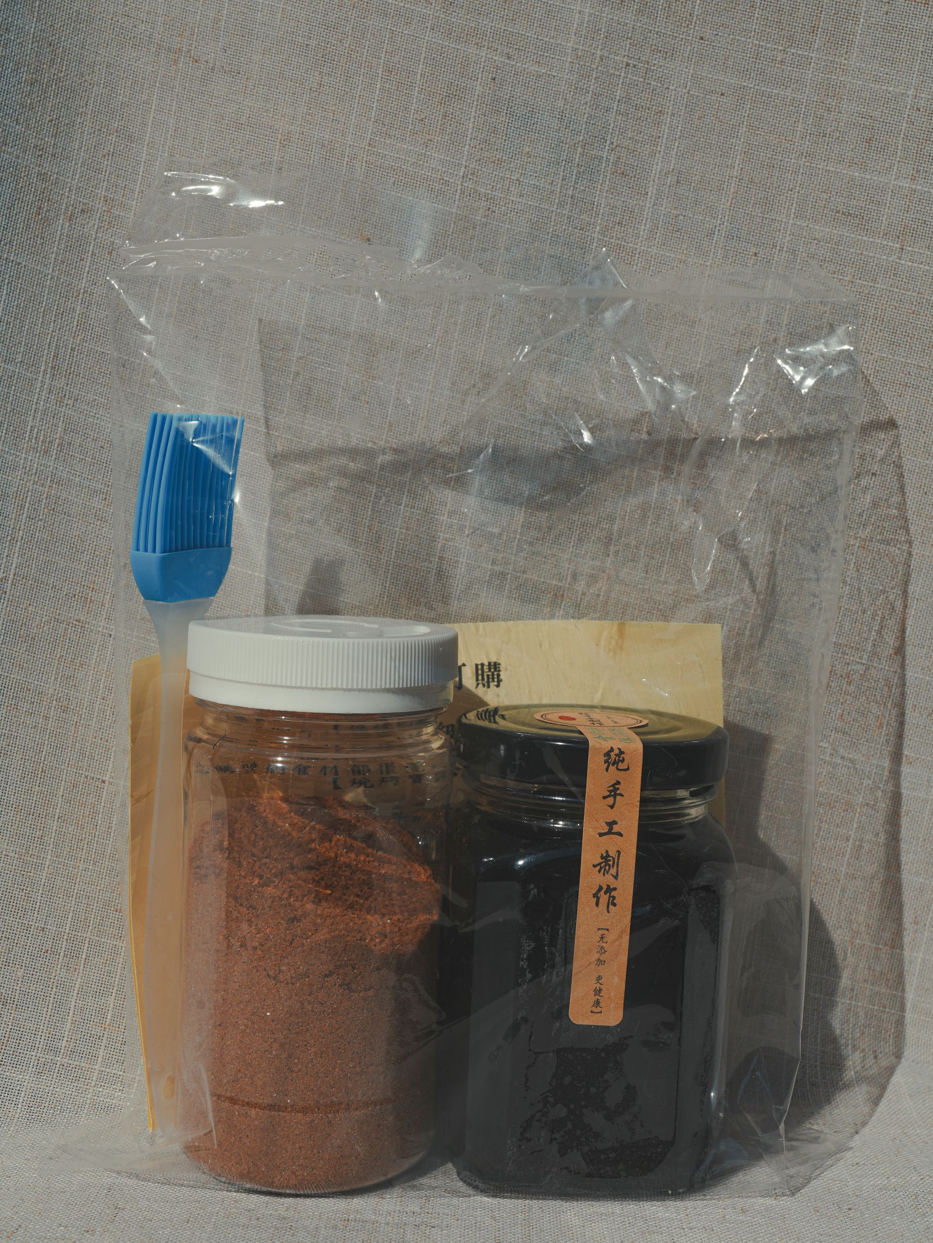 幾罐深色液體，一碗紅棕色粉末，以及另一個裝有粉末的容器和一把小刷子，都放在一個平面上。