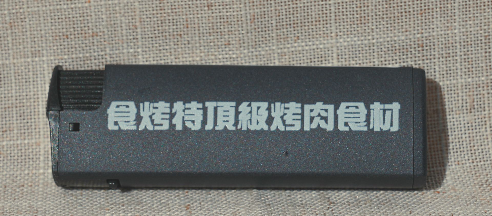 黑色打火機，米色表面印有白色中文「頂級燒烤食材」。