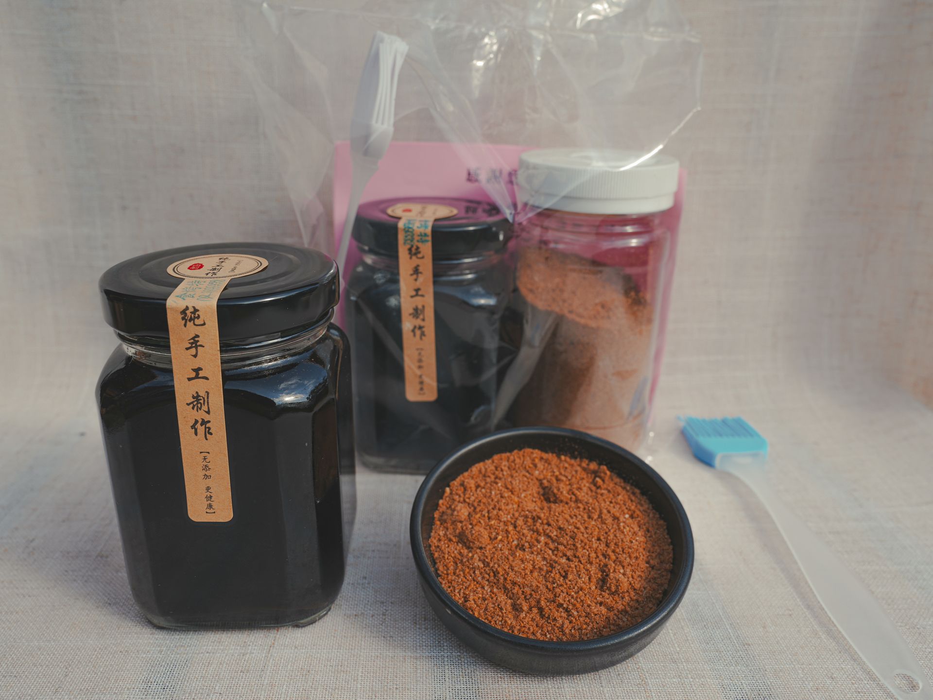 幾罐深色液體，一碗紅棕色粉末，以及另一個裝有粉末的容器和一把小刷子，都放在一個平面上。