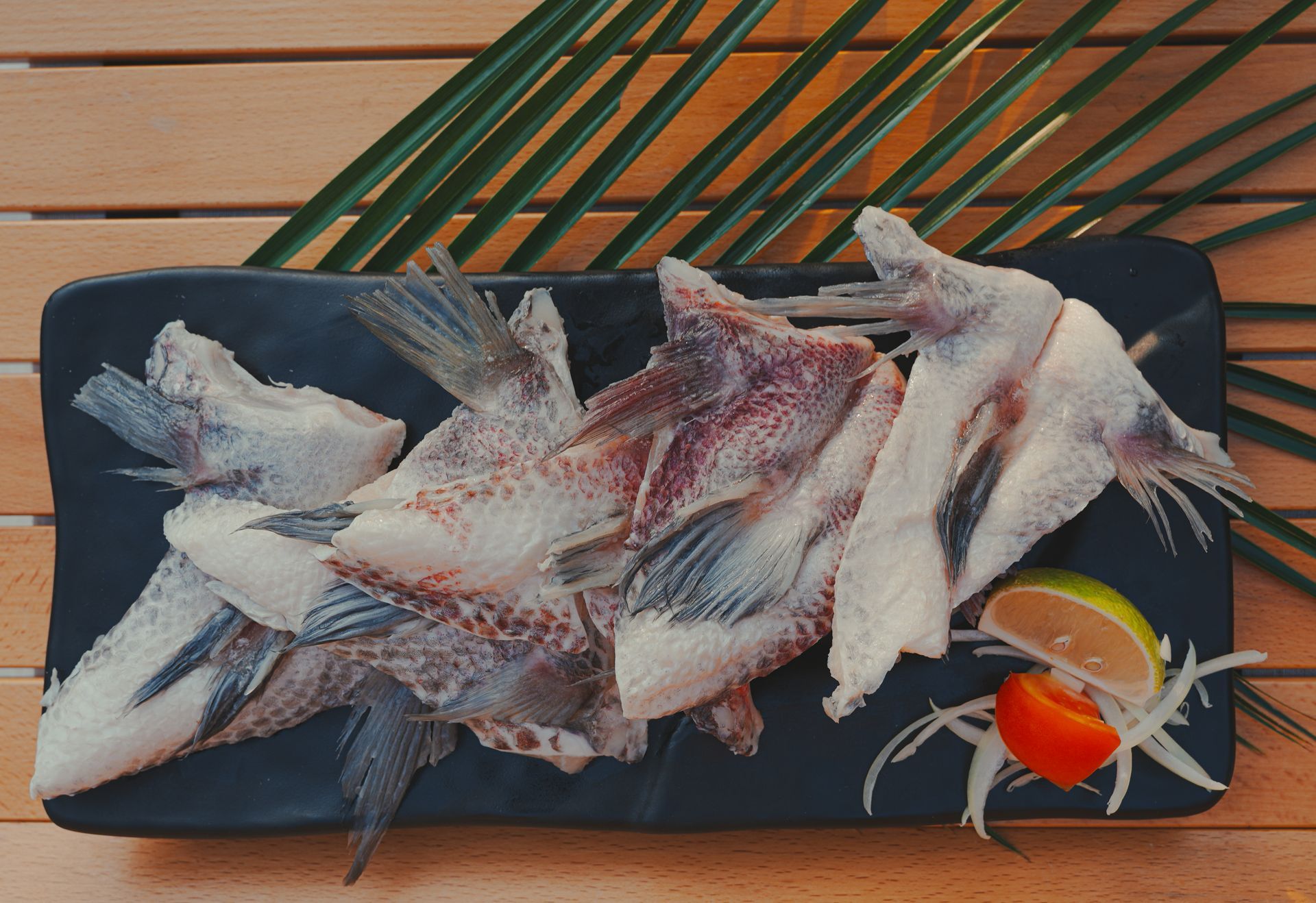 幾片生魚片，魚尾清晰可見，放在黑色盤子上，配上青檸、番茄和洋蔥。