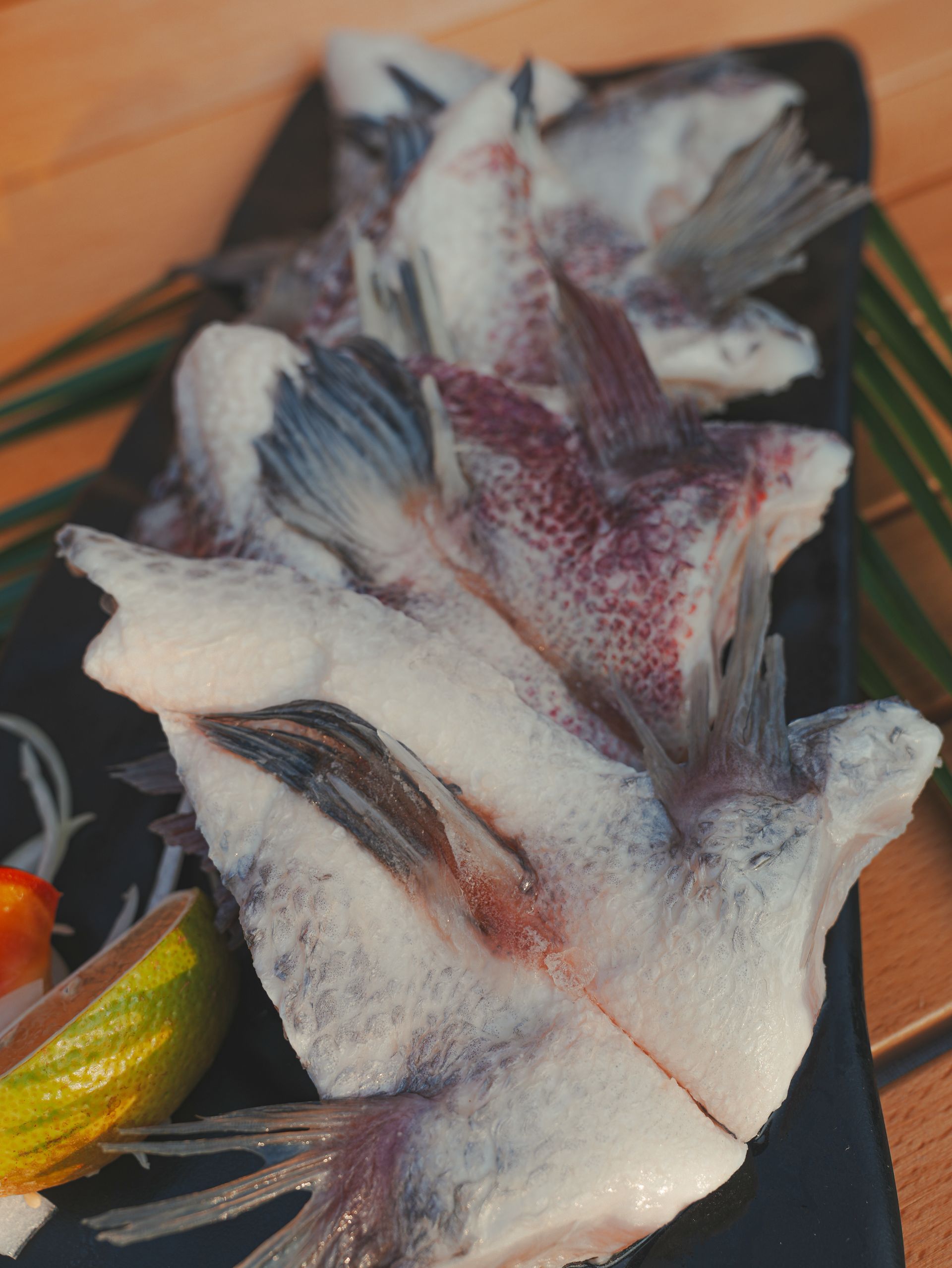 幾片生魚片，魚尾清晰可見，放在黑色盤子上，配上青檸、番茄和洋蔥。