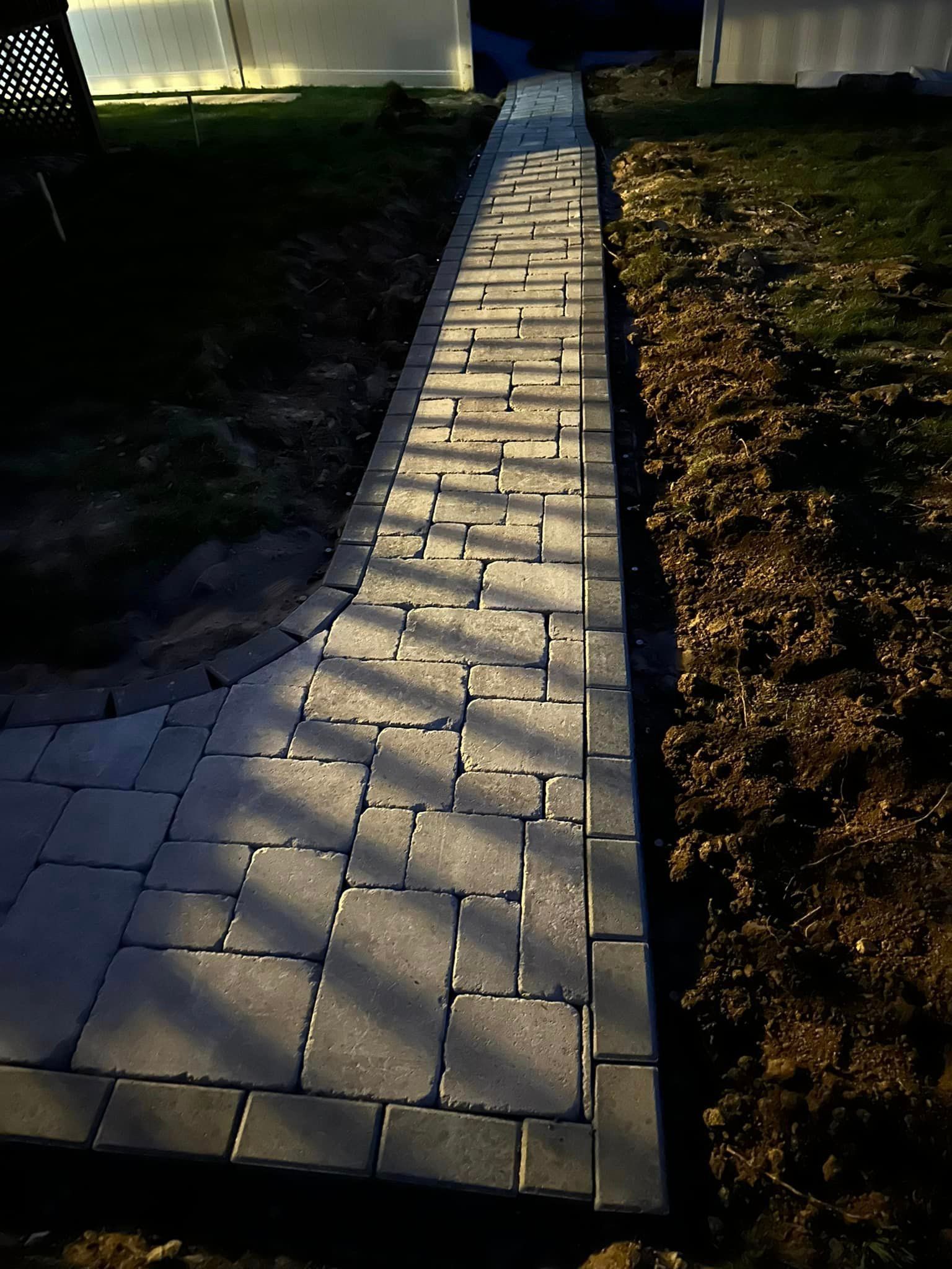 A brick walkway leading to a house with a greenhouse in the background