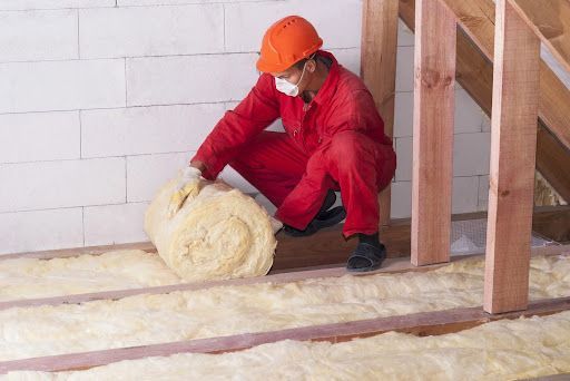 Crawl space insulation installer placing fiberglass insulation.