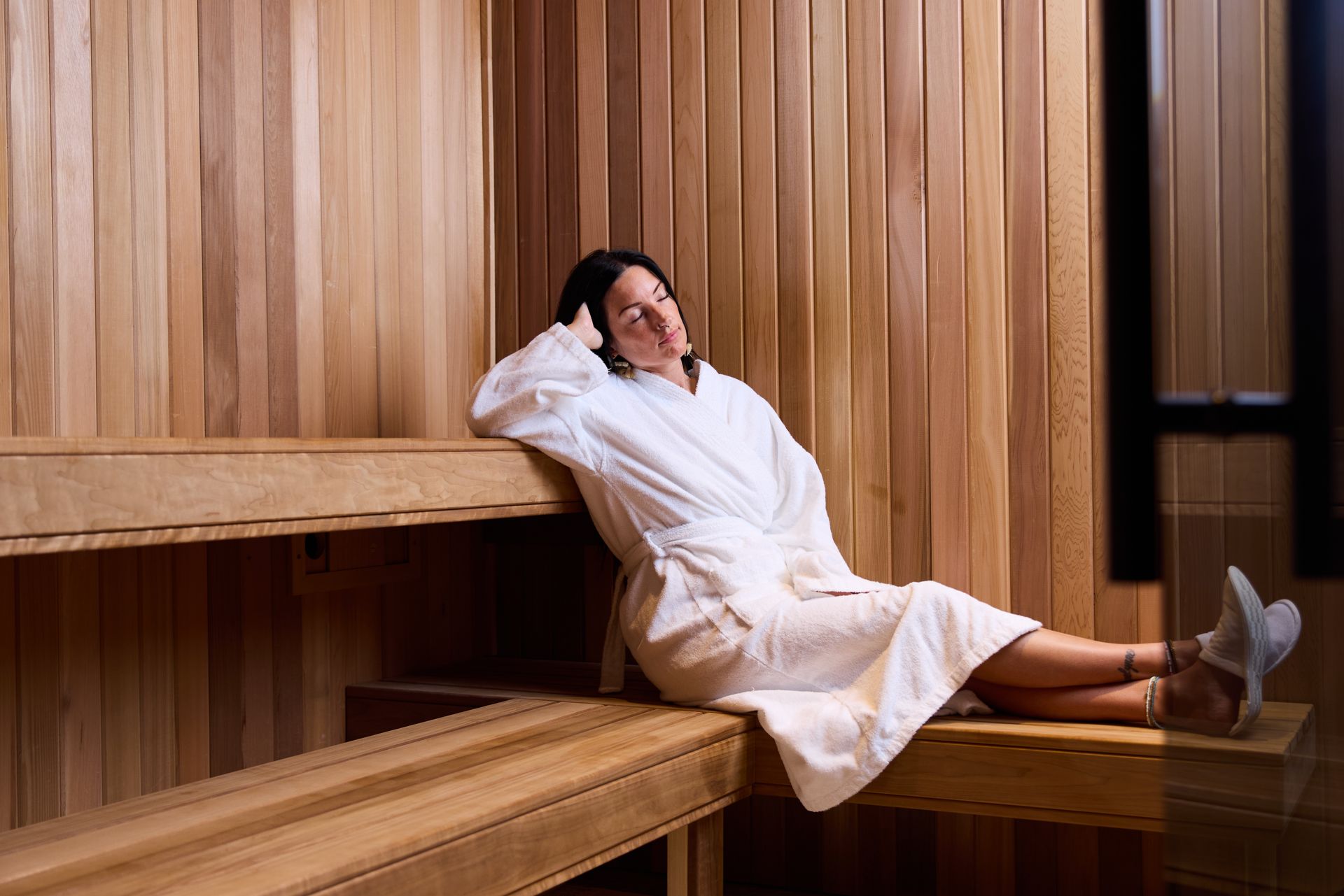 Woman in a white robe sitting down in a sauna