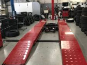 Red car lift in a tire shop with tires stacked around.
