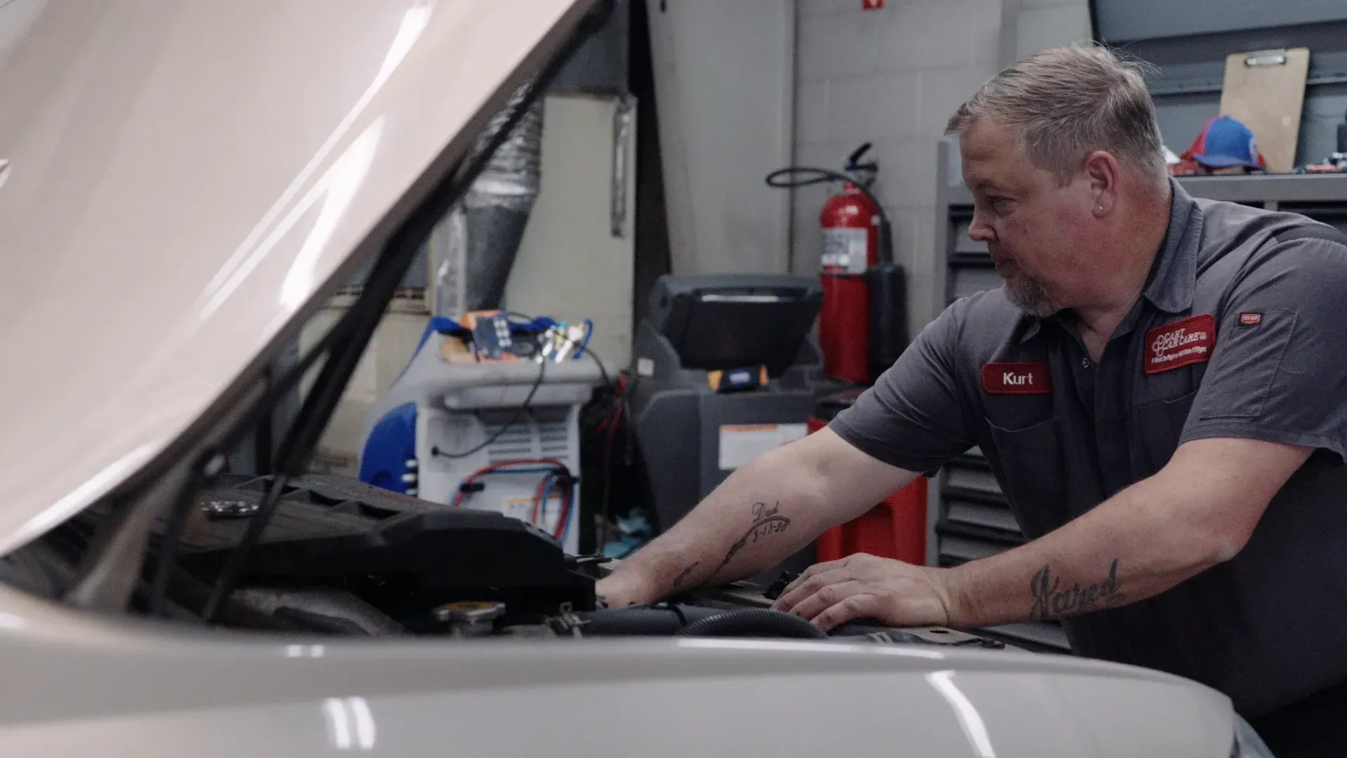 Mechanic in a gray shirt working on a car engine in an auto shop.