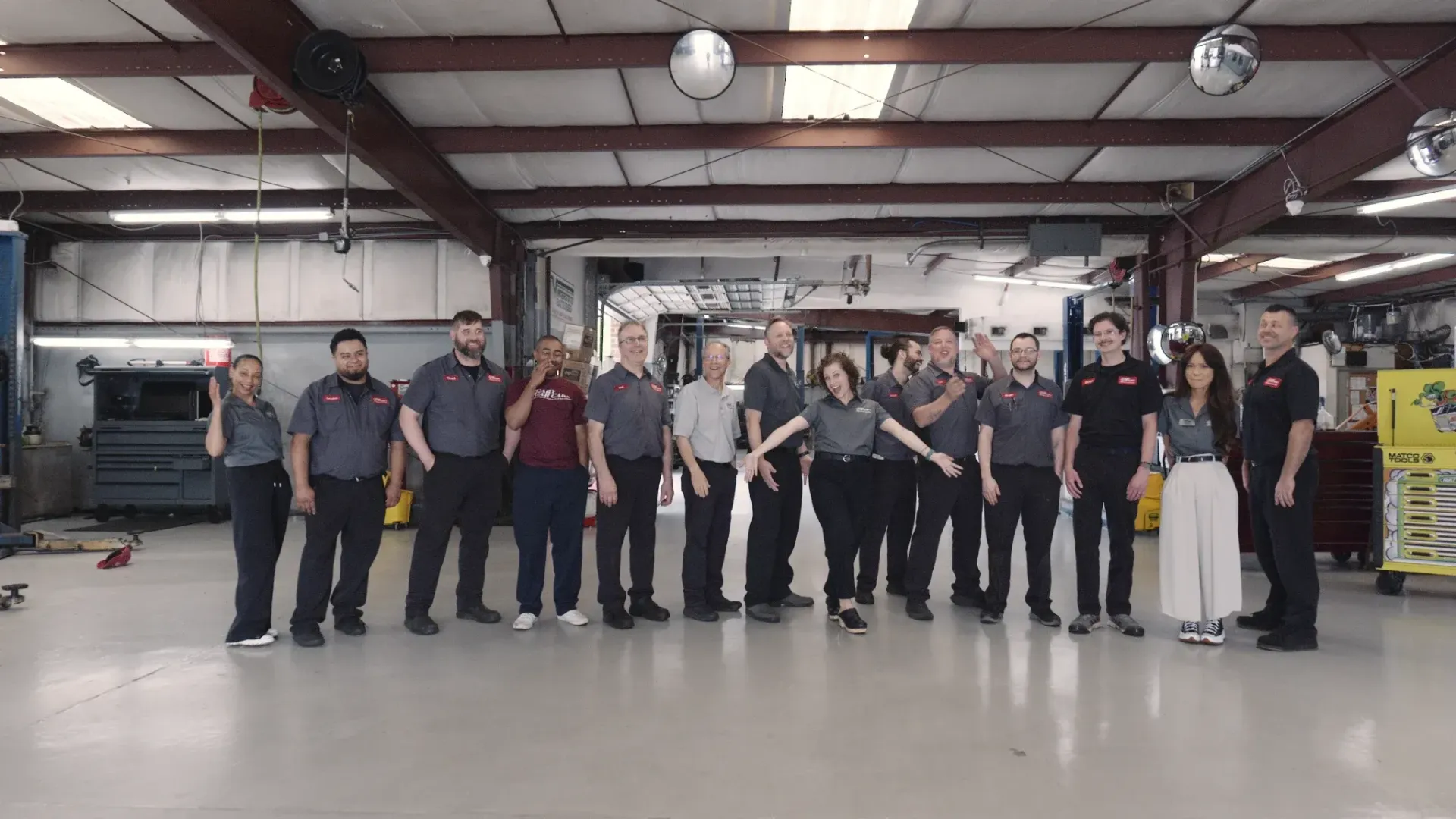 Group of auto shop employees posing inside the garage, with arms outstretched.