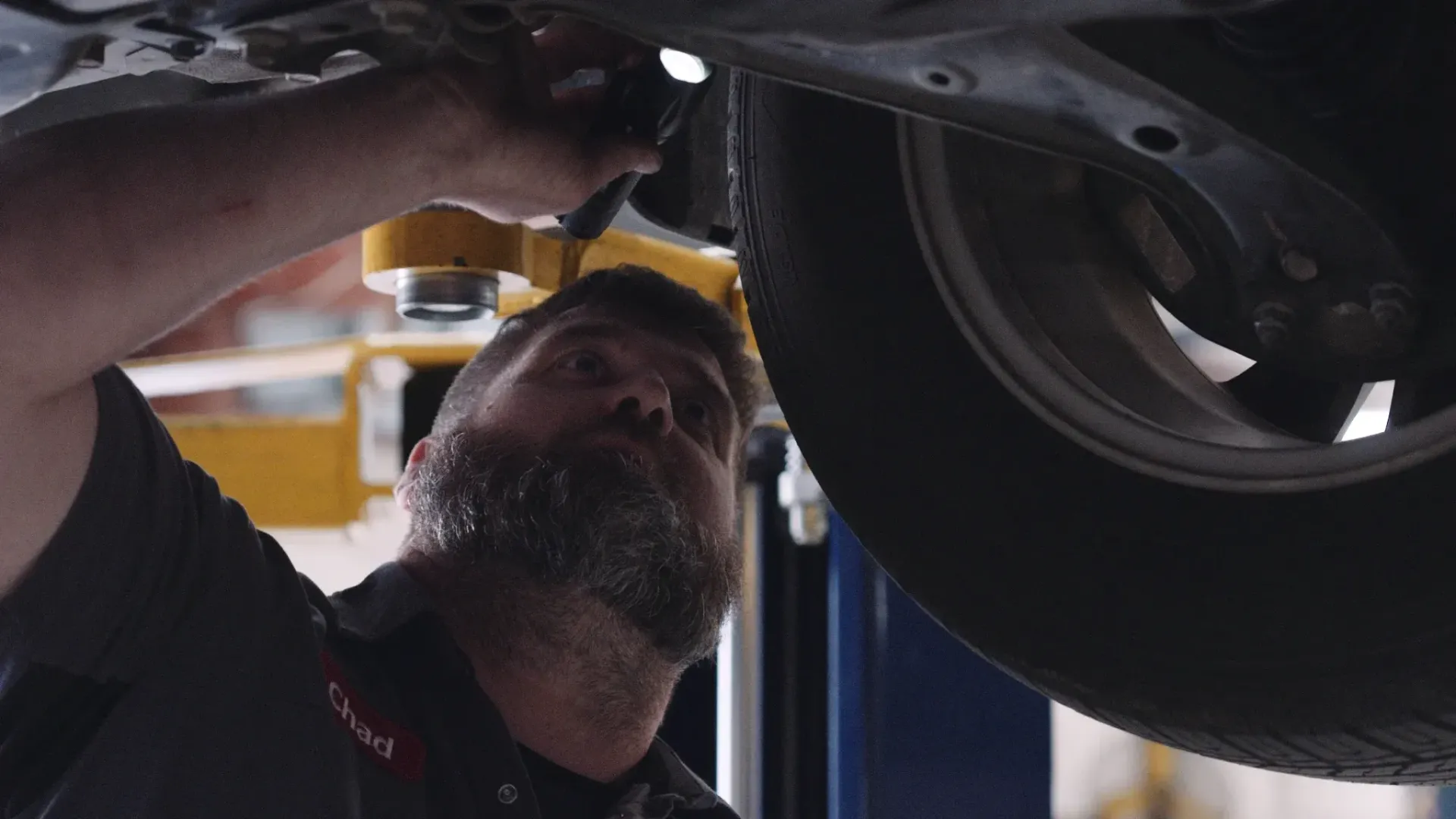 Mechanic working under a car, illuminated by a yellow light, in a garage.