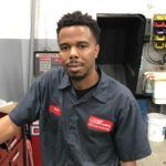 Mechanic in blue uniform at auto shop, looking at the camera.