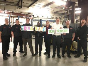 Group of eight people in a garage holding signs that spell 