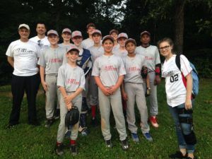 Baseball team posing outdoors; players in gray uniforms, coaches in white shirts.