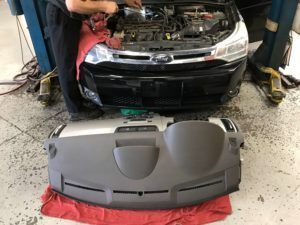 Car with open hood, mechanic working on engine. Dashboard removed and placed on the floor in front of the car.
