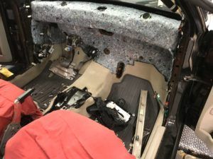 Interior car view with dashboard and components removed, exposing insulation and wiring.
