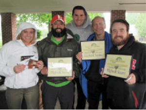 Group of five people holding certificates, smiling, possibly at an outdoor award ceremony.