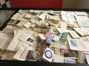 A glass-covered display of scattered letters, cards, and printed material, likely archival documents.