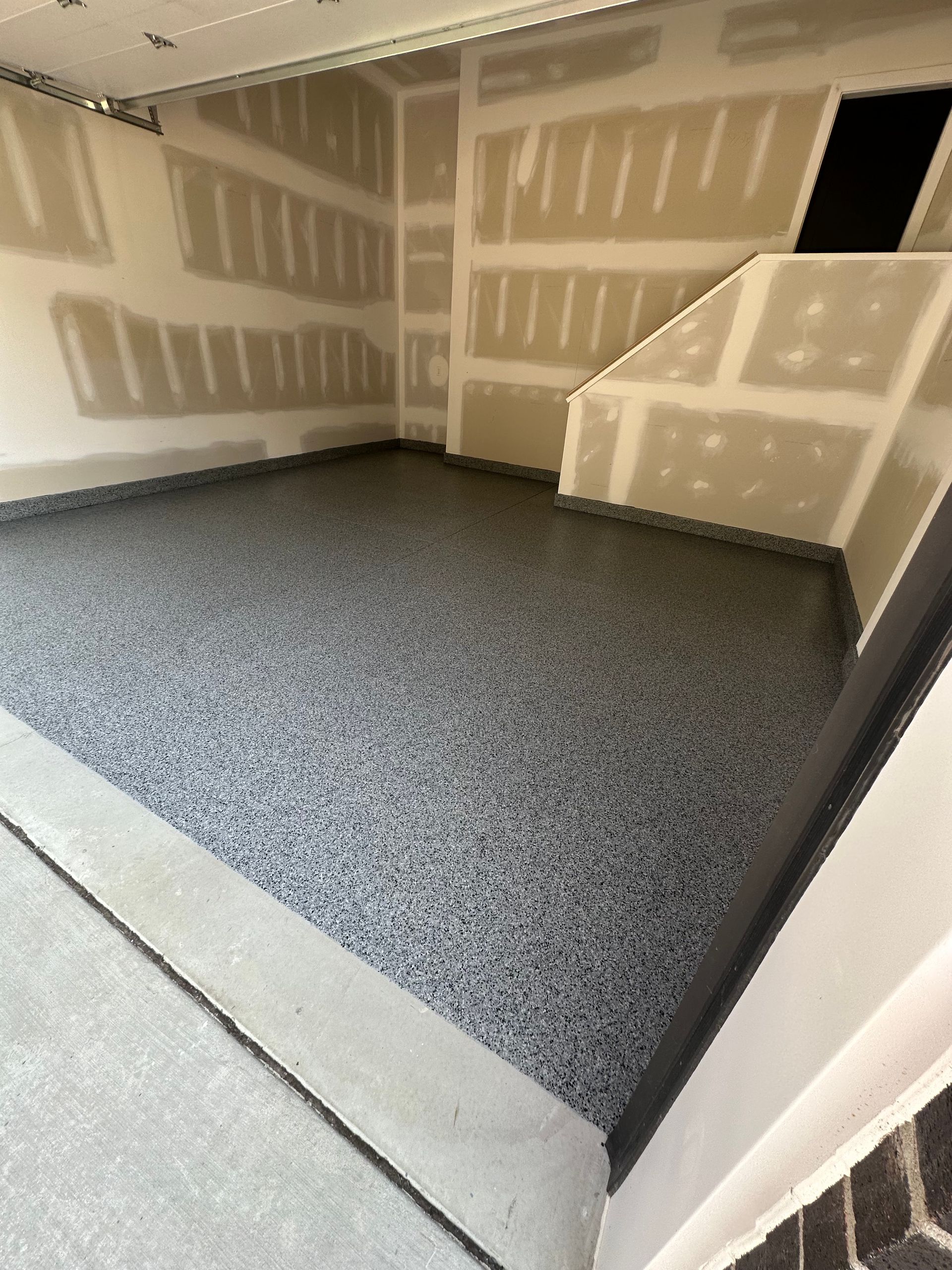 Empty unfinished room with drywall, gray carpet, and a concrete floor at the entrance.
