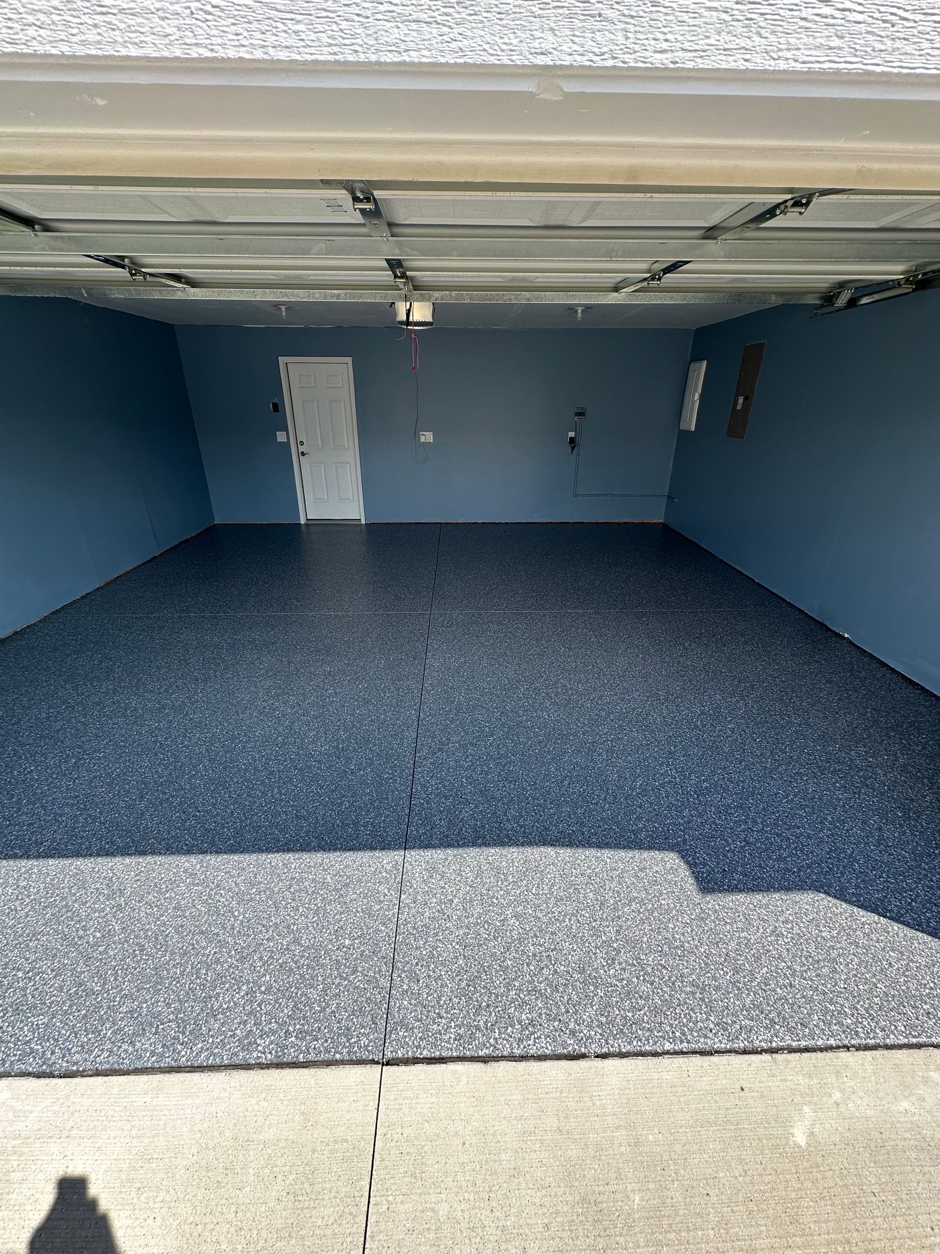 Empty blue garage with speckled floor and open door, viewed from the driveway.