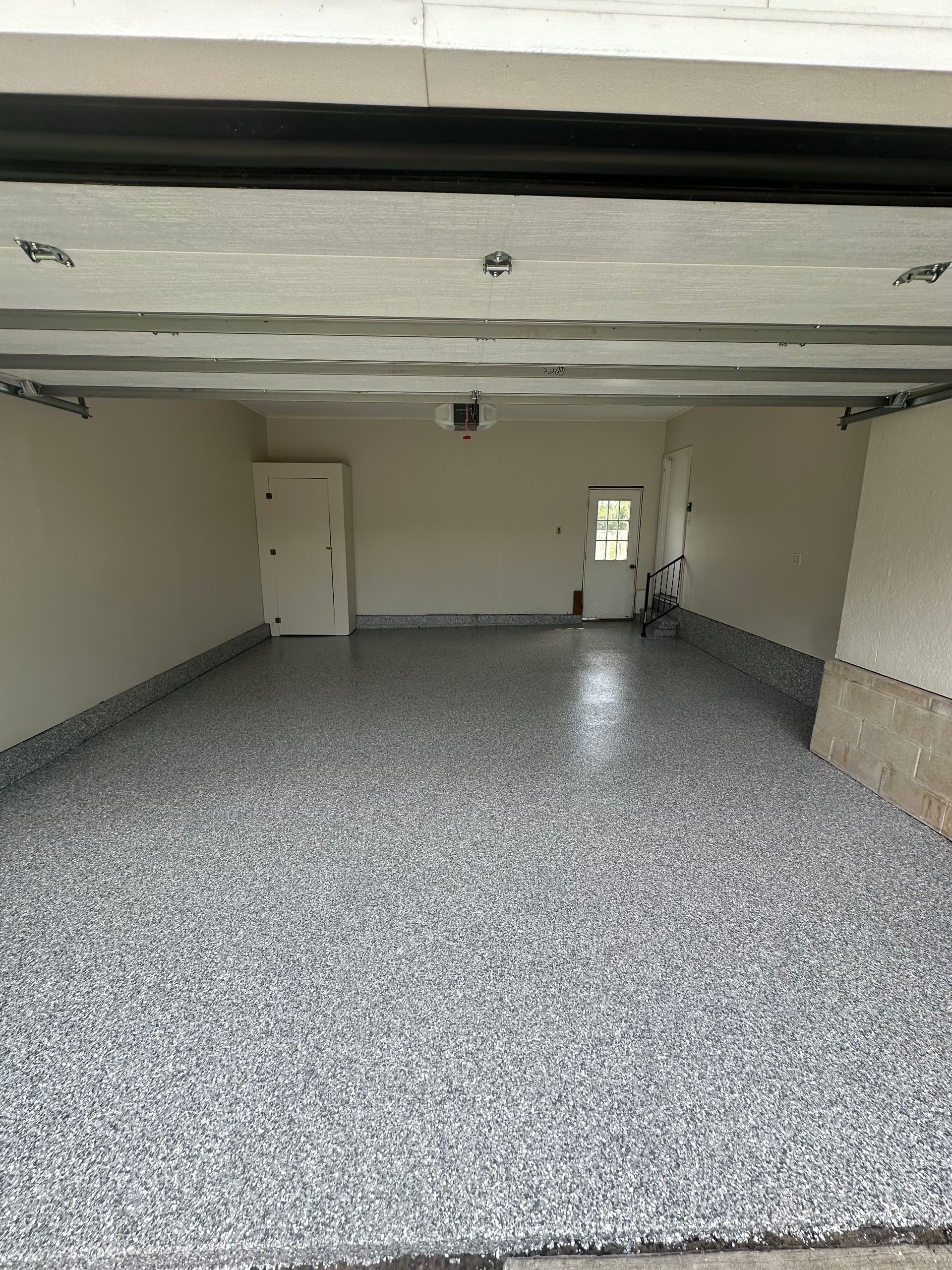 Empty garage with speckled floor, white walls, overhead beams, and a small back window.