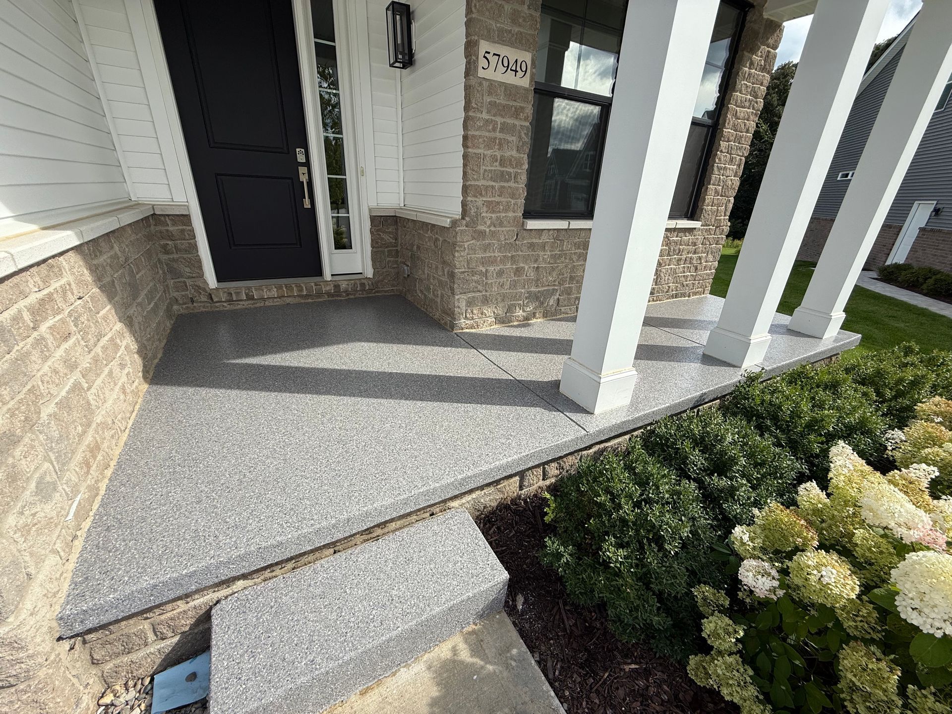 Front porch with concrete ramp, black door, white columns, and flower bed beside the entryway.