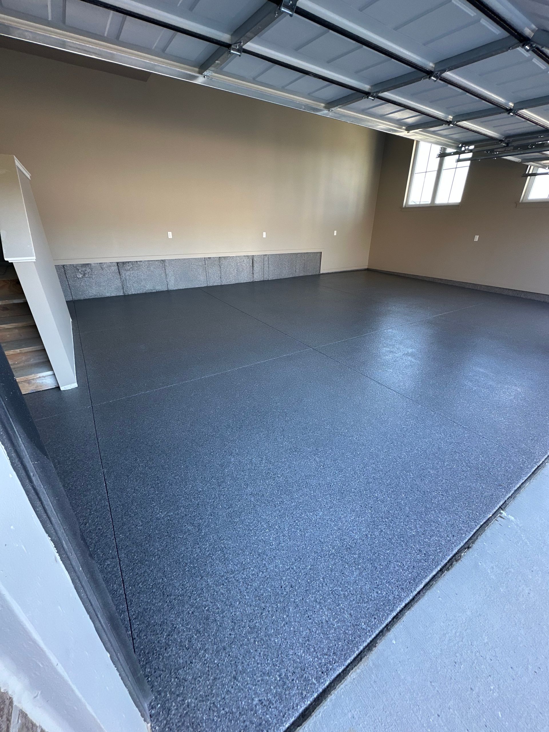 Empty garage with speckled gray floor, beige walls, and open ceiling beams.