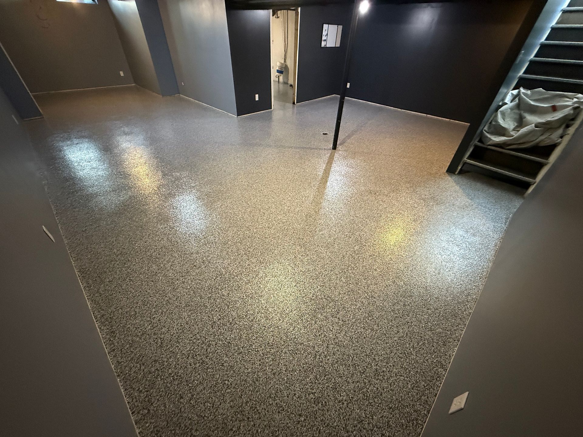 Empty hallway with speckled floor, dark walls, and an open door at the far end