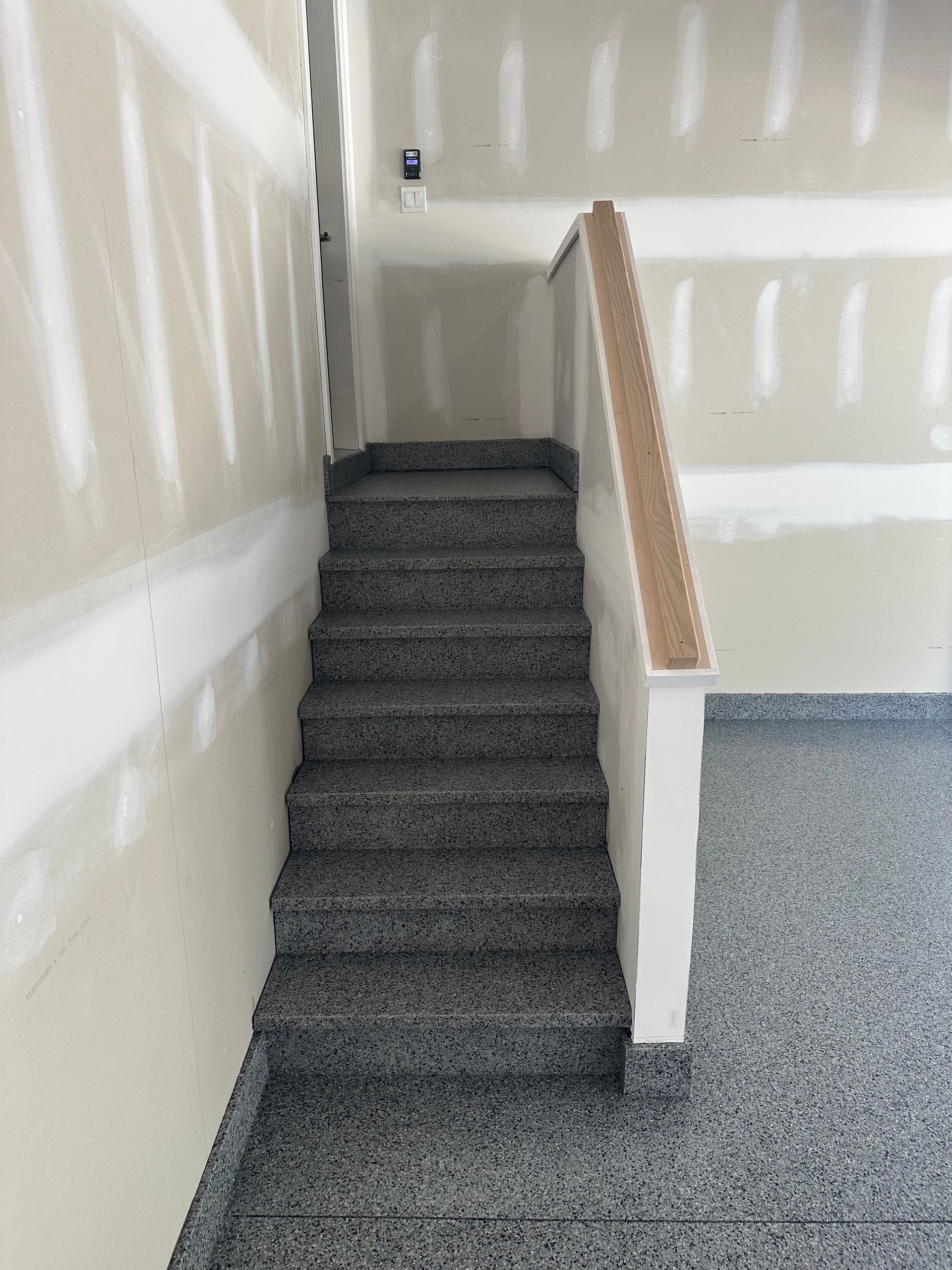 Carpeted indoor stairway with white walls and a wooden handrail, leading to a landing.