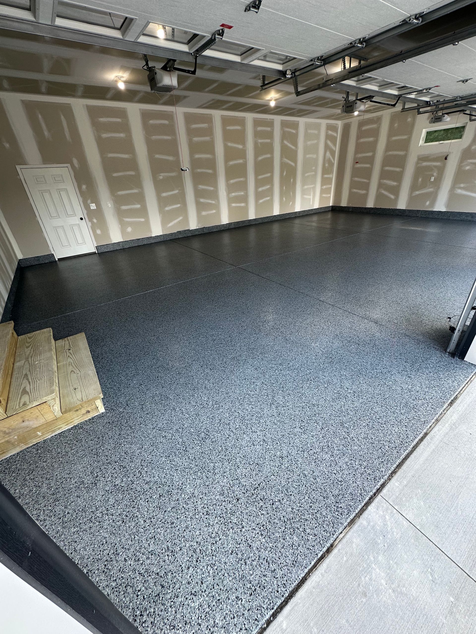 Empty garage interior with gray epoxy floor, beige walls, and overhead lights