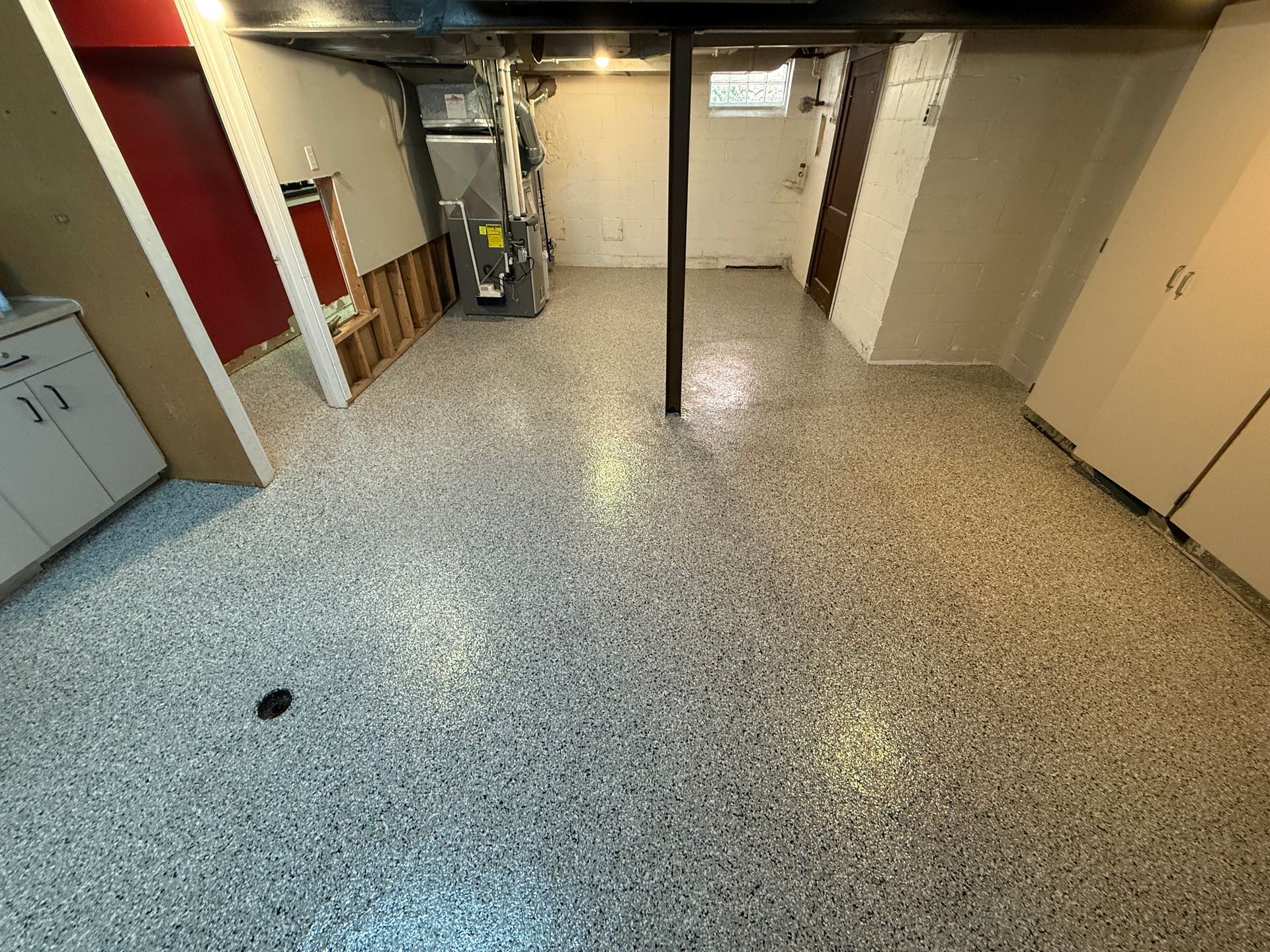 Basement utility room with speckled floor, support pole, washer, and cabinets along the walls.