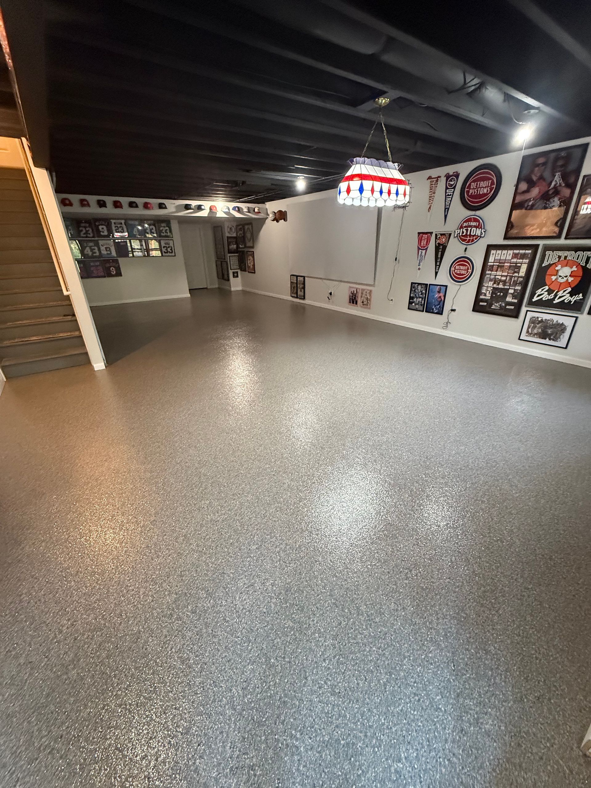 Empty game room with speckled floor, black ceiling, wall art, and a hanging red-and-white light fixture.