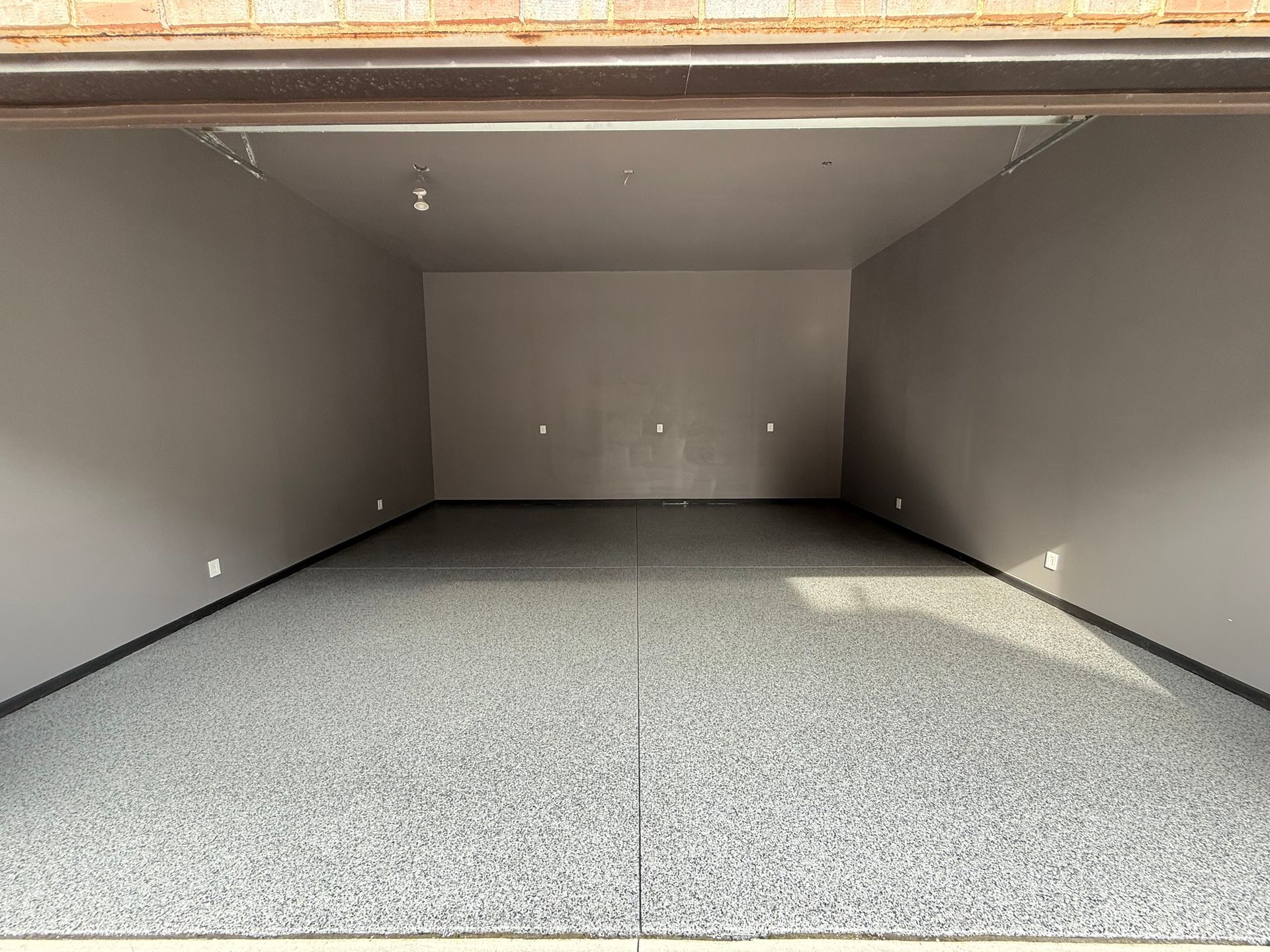 Empty gray garage with speckled floor and a small back wall opening
