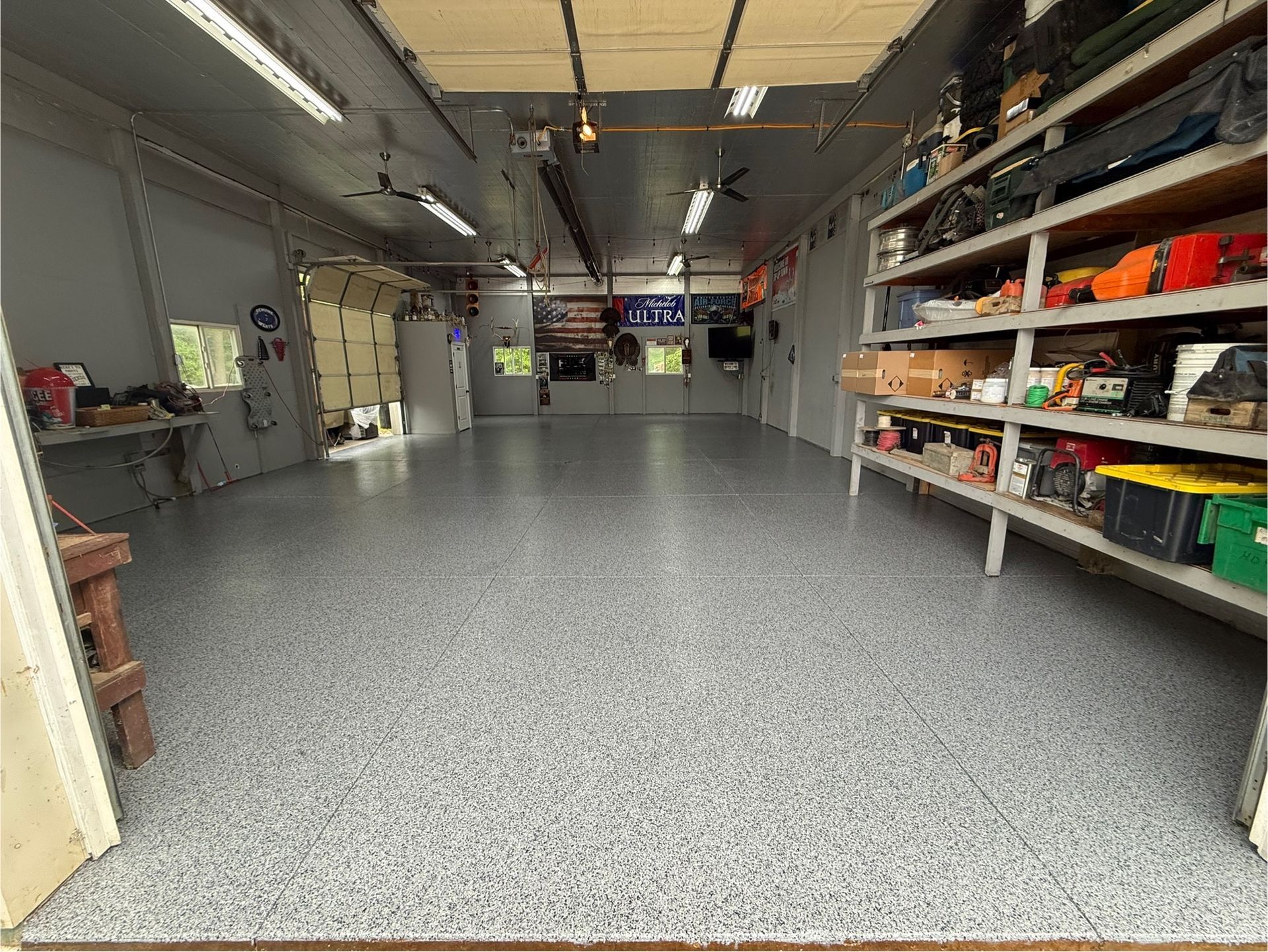 Empty workshop with gray speckled floor, shelves of supplies, and fluorescent ceiling lights