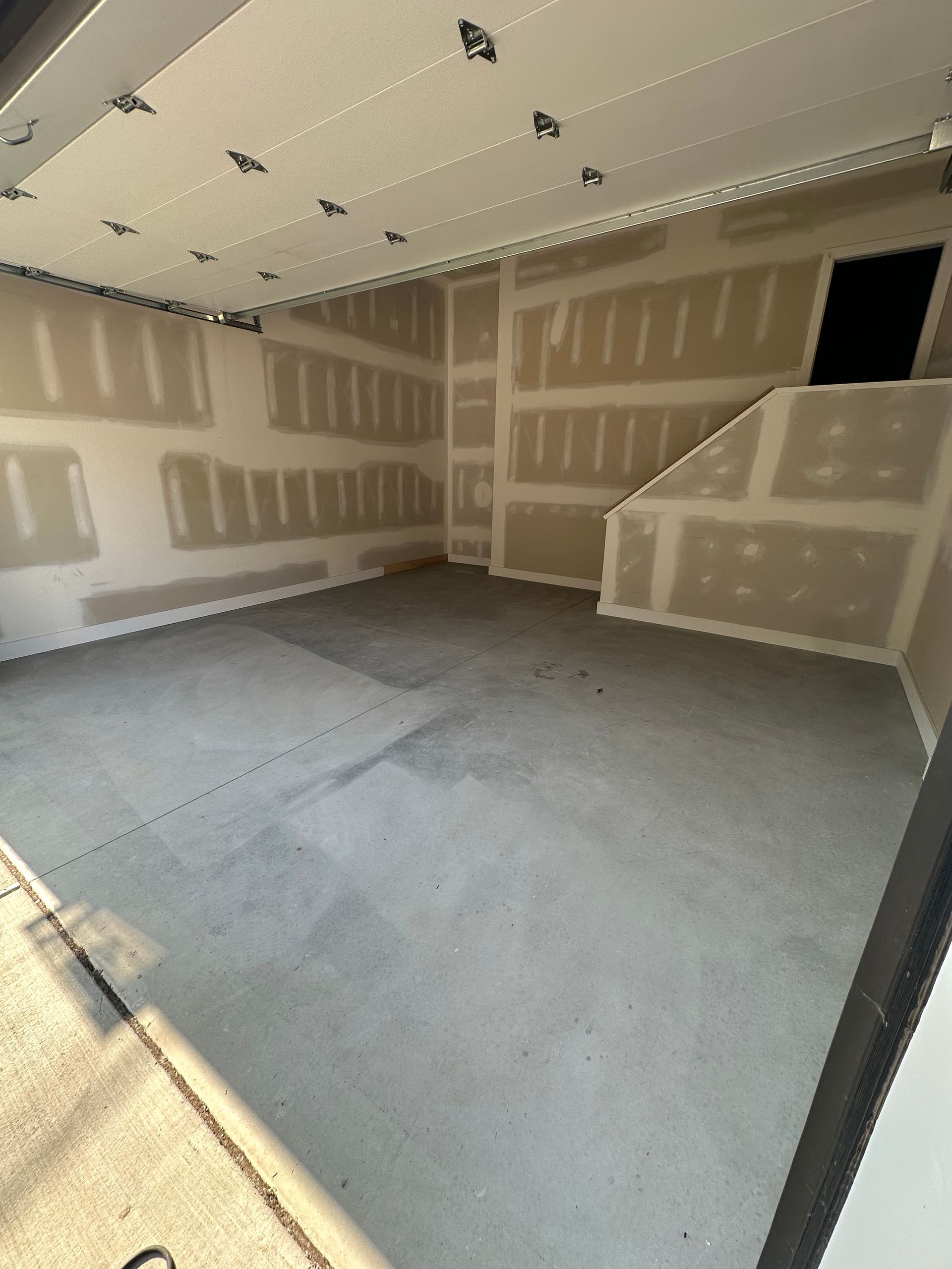 Empty unfinished garage with drywall, gray floor, and a small stair/ledge area.