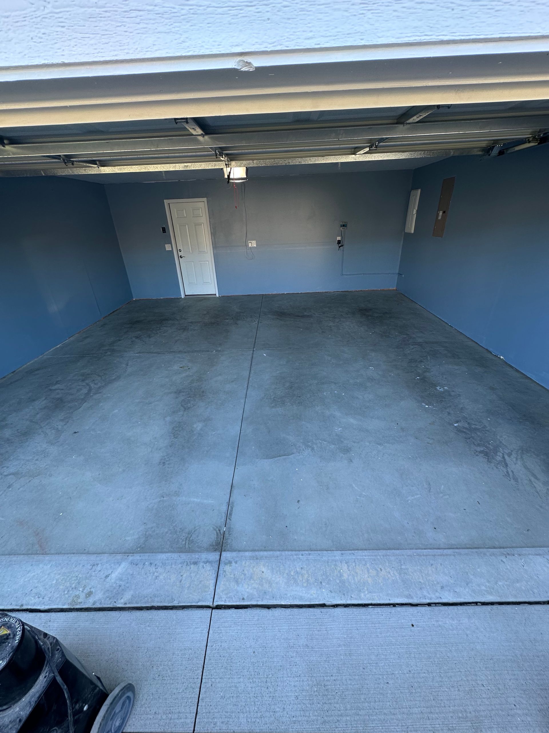 Empty blue garage with concrete floor and low ceiling, viewed from the back toward the open front.